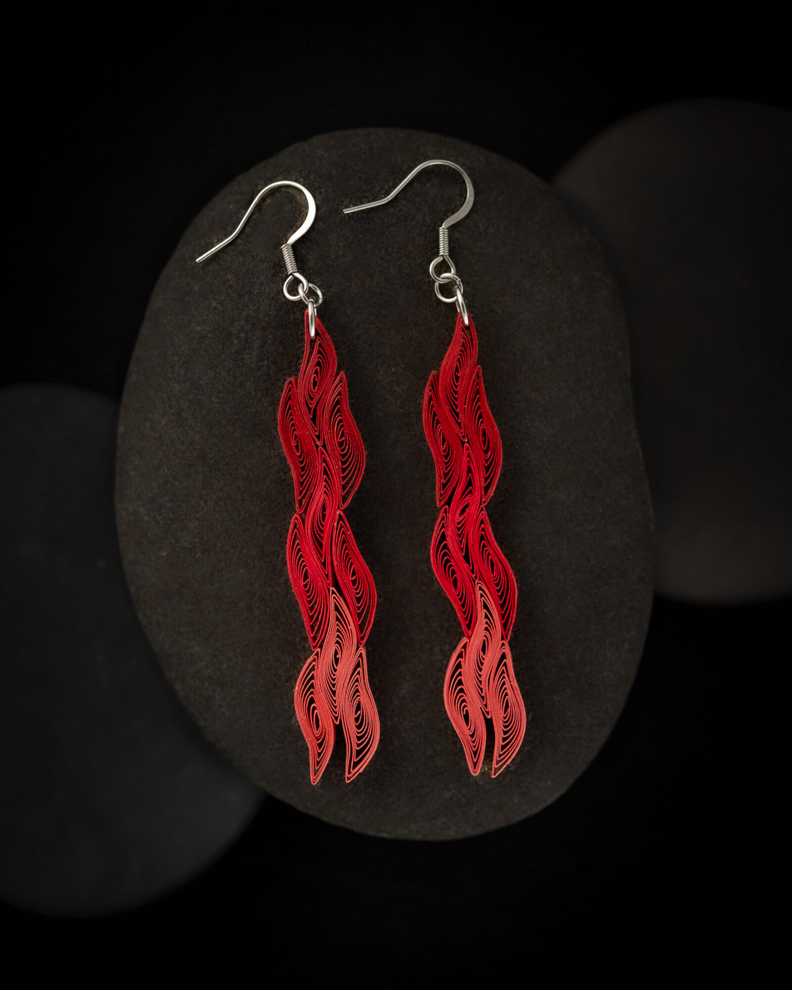 Red dangling earrings with wavy design on black background, displayed on a black oval surface.