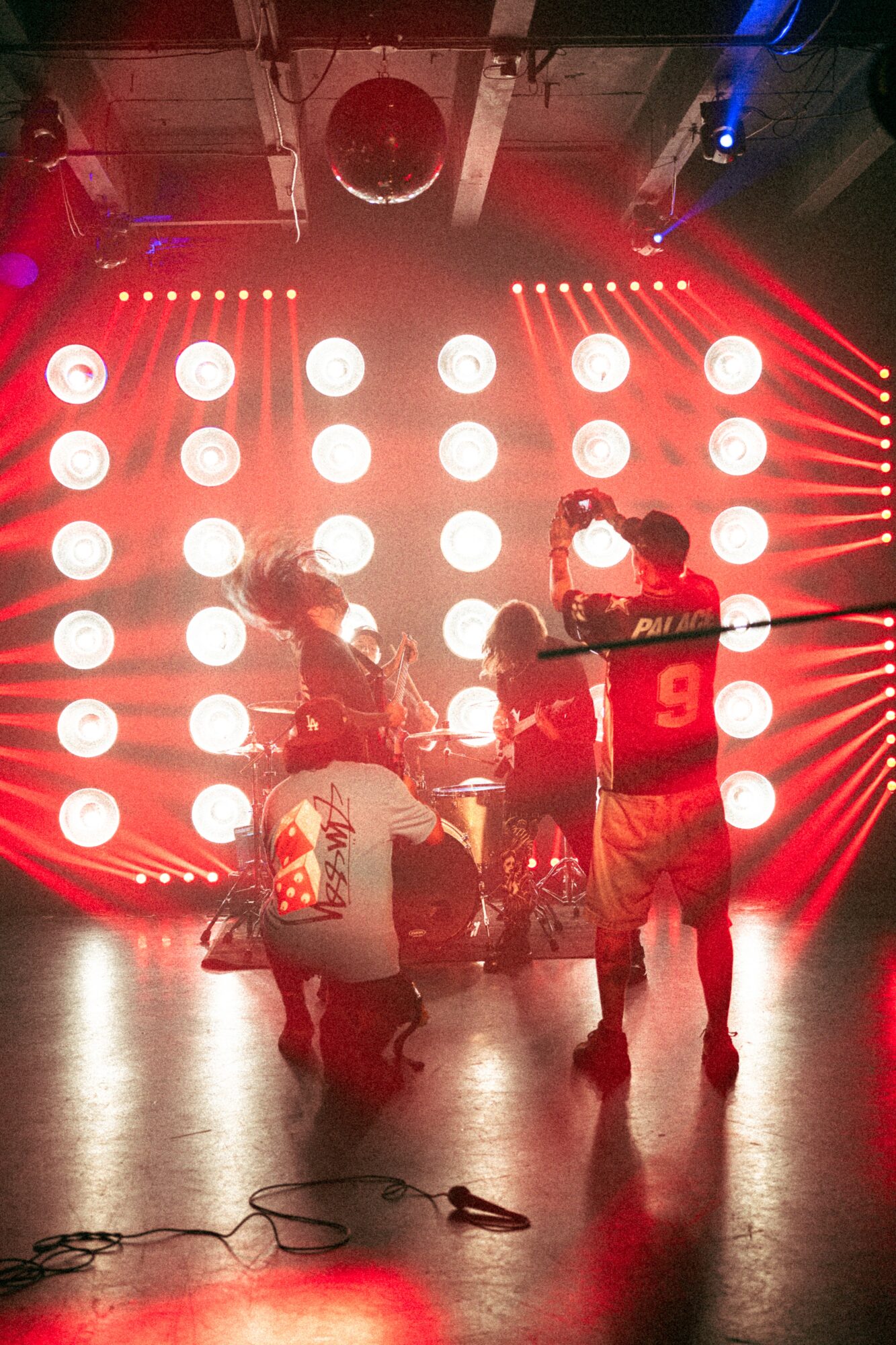 Group of people on stage with bright circular lights and red laser beams in the background, performing or preparing for a show.