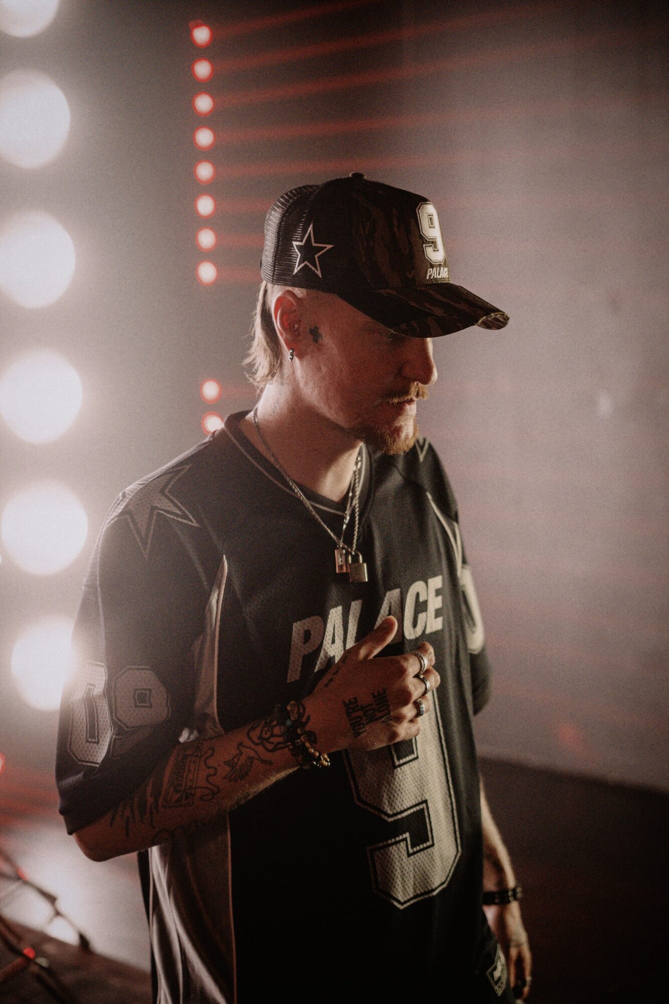 Person wearing a cap and sports jersey, holding a microphone, with stage lights in the background.