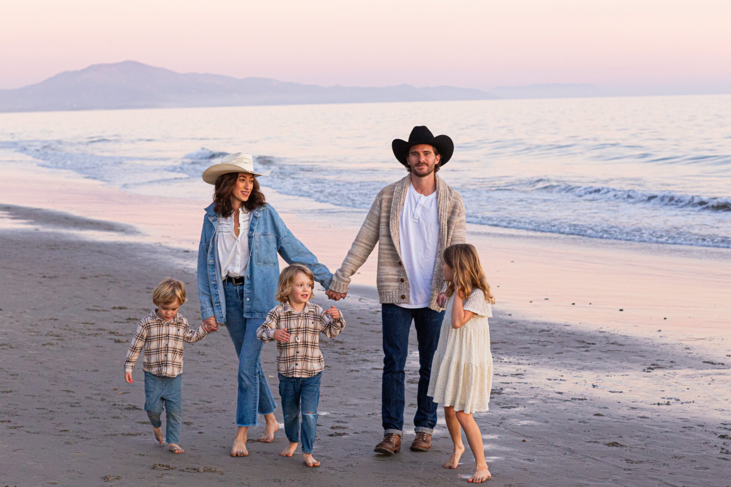 Family walking on the beach holding hands, with children and adults, during sunset or sunrise.