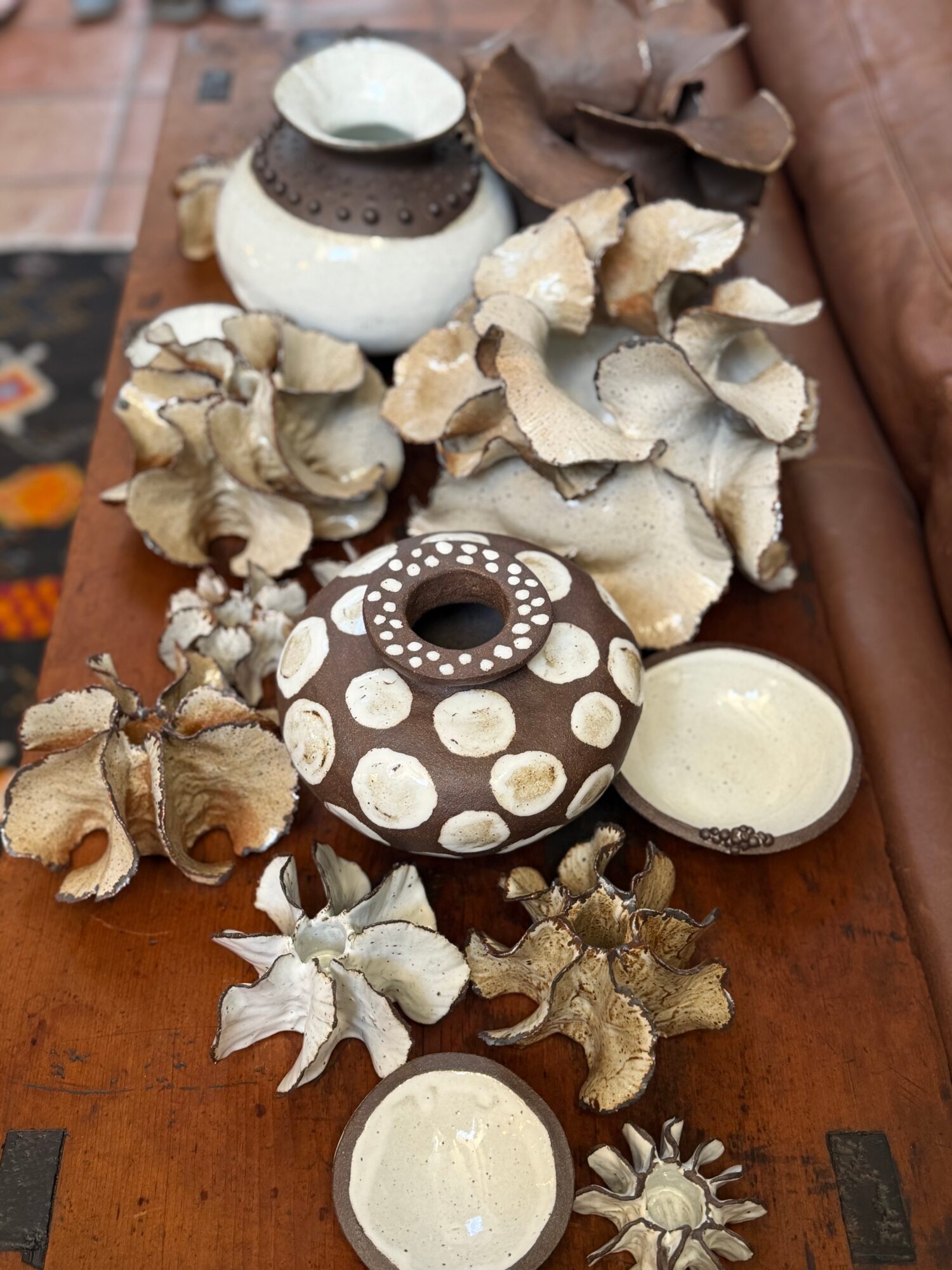 Decorative pottery and dried plant arrangements on a wooden surface, including a round vase with white dots, small bowls, and dried leaves.