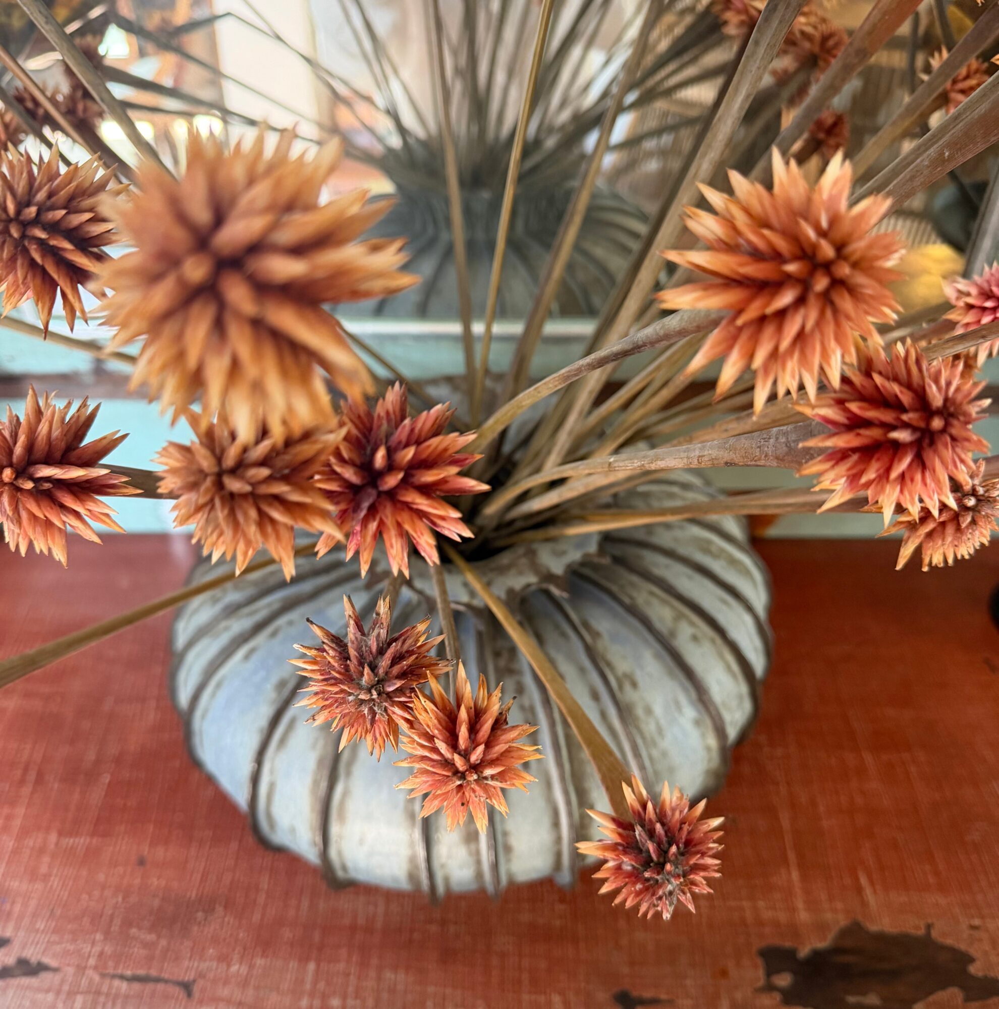 Dried orange and brown flowers in a striped ceramic vase on a wooden surface.
