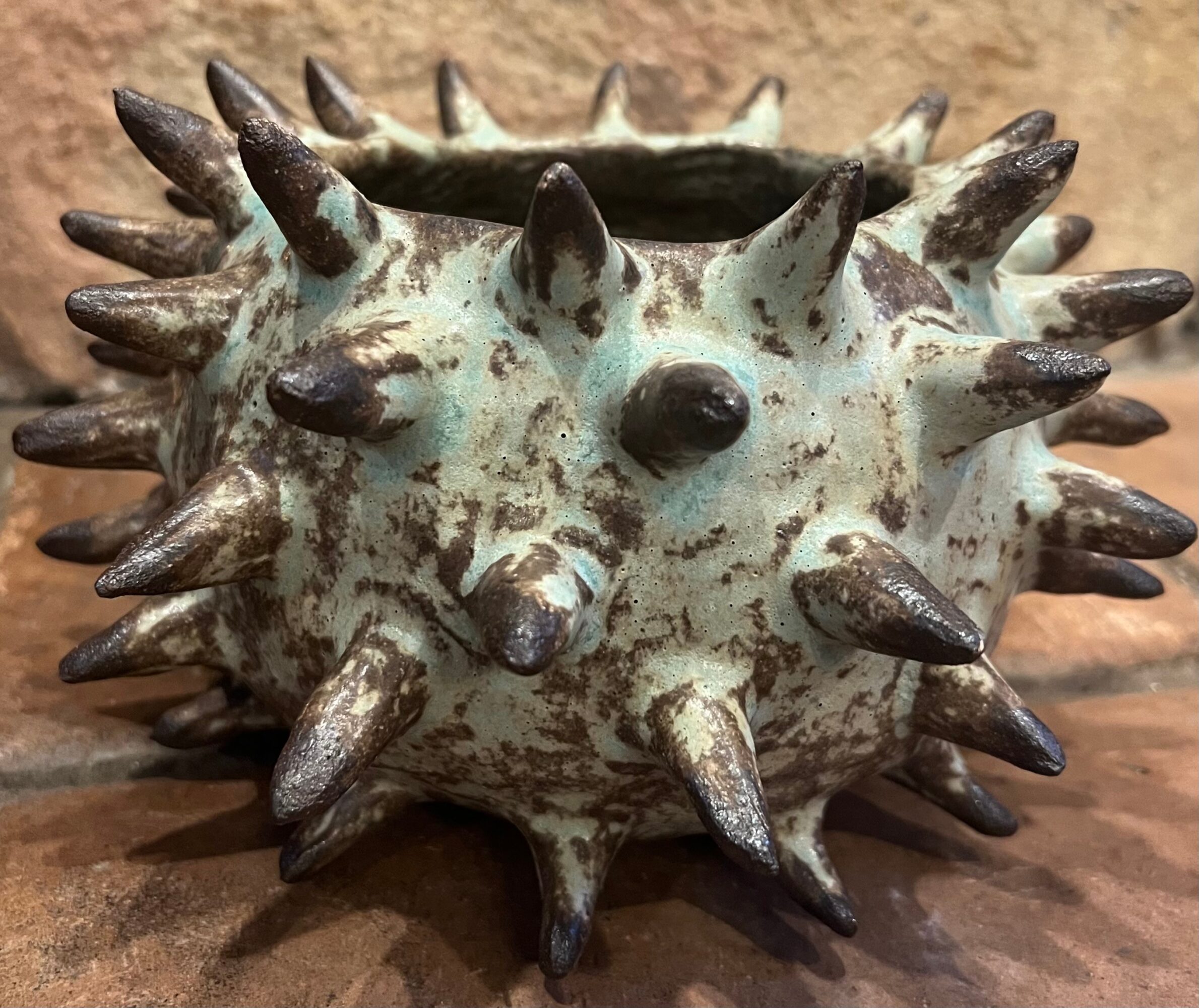 A spiked ceramic pot with a hedgehog design, featuring a textured surface and multiple pointed spikes, on a wooden surface.