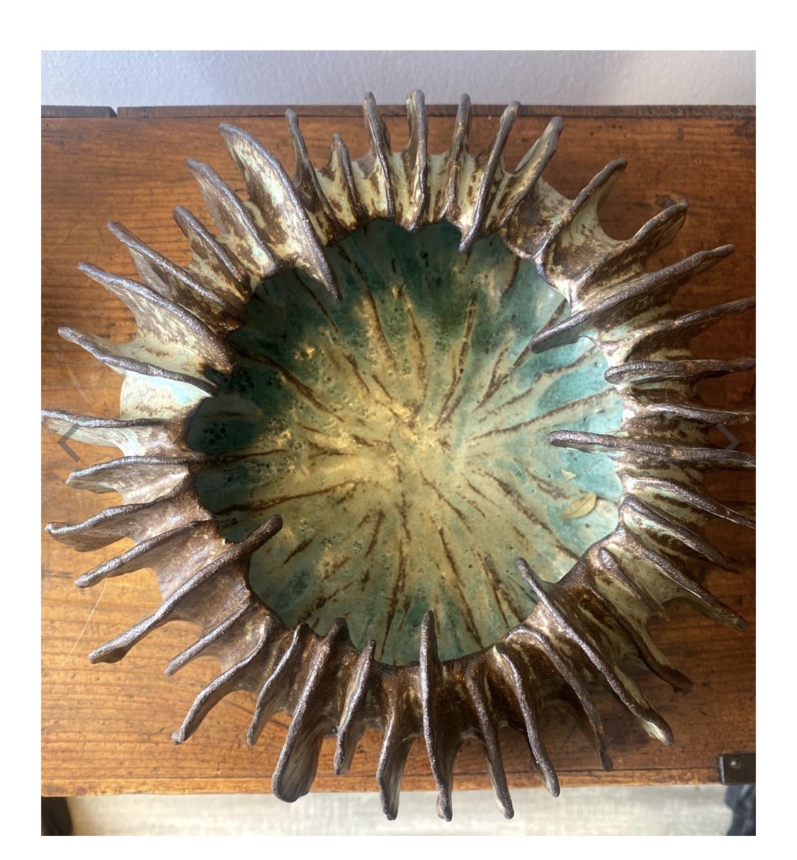 Circular metal sculpture with spikes radiating outward, mounted on a wooden surface.