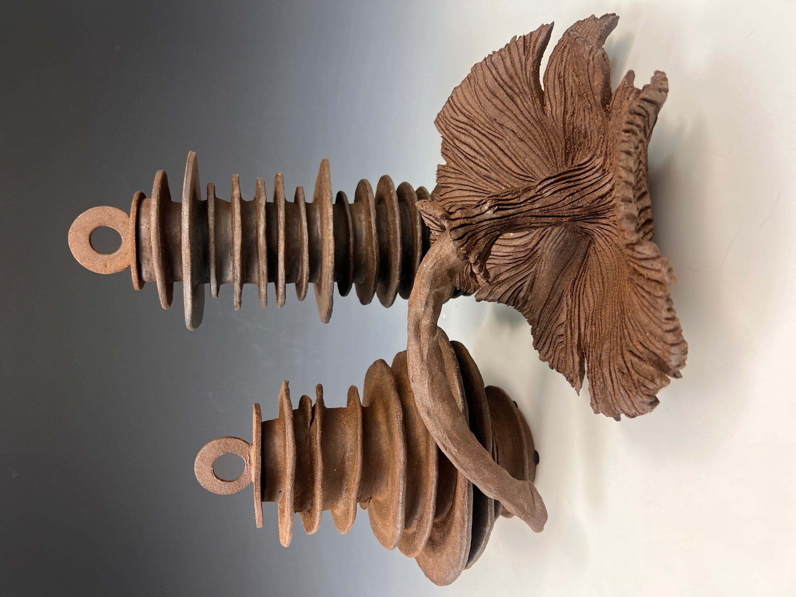 Wooden sculpture of a mushroom with a textured cap and stem, placed on a white surface.