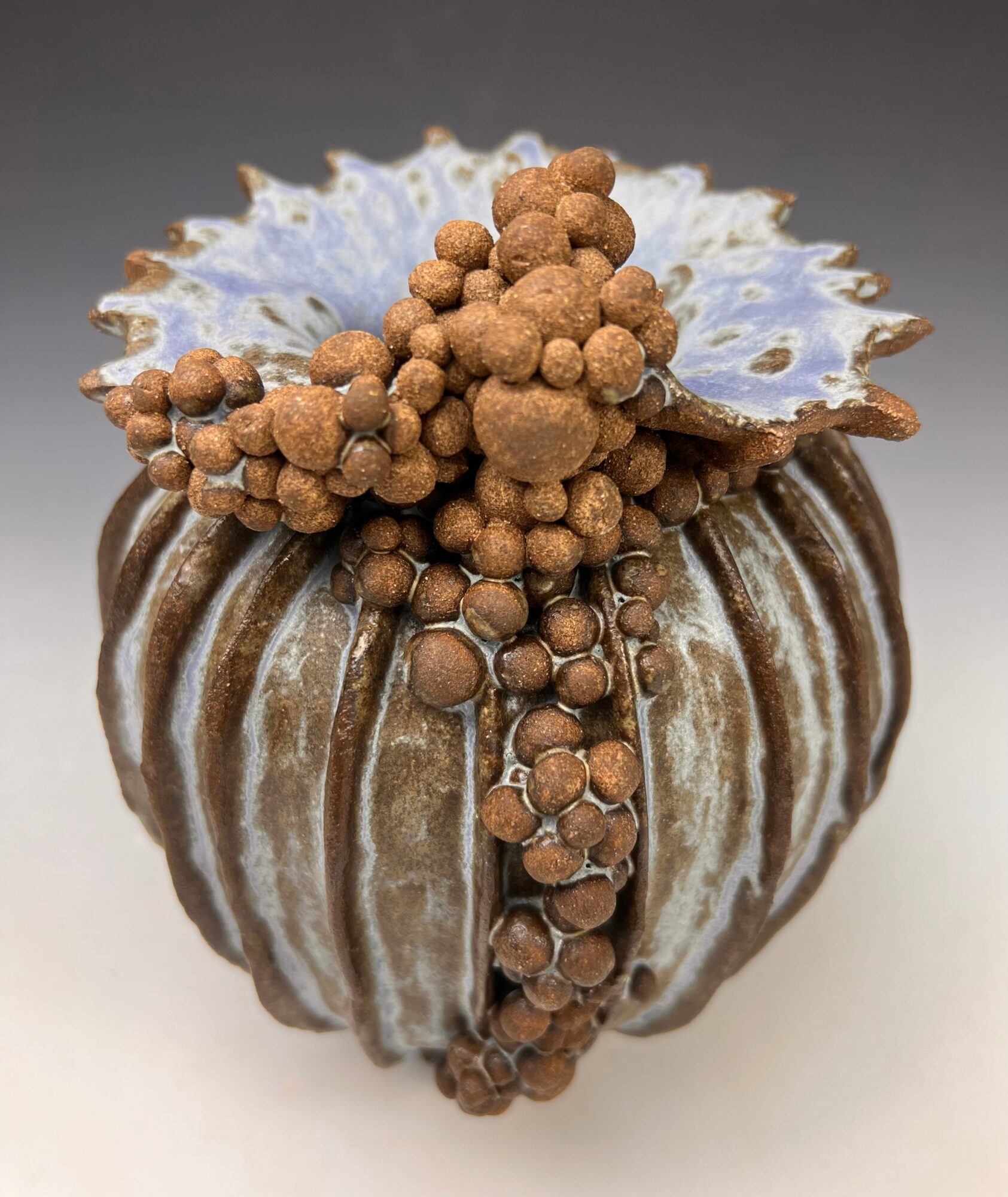 Decorative pumpkin with brown and white striped surface, topped with brown and blue textured elements, against a neutral background.