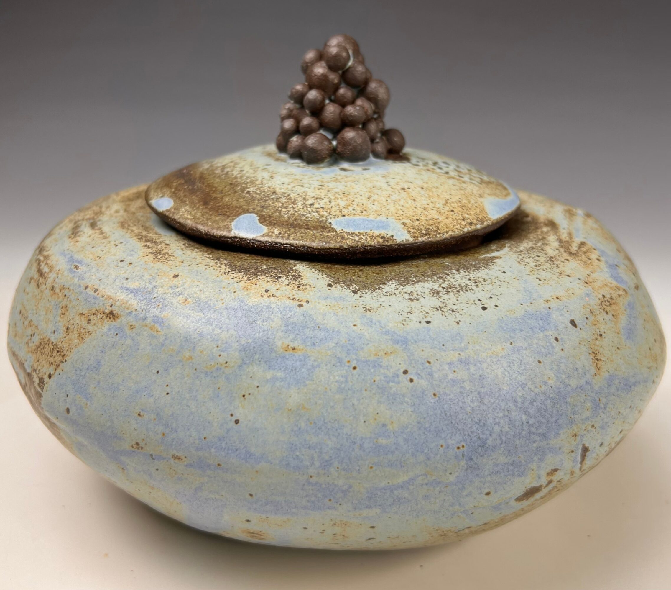 Ceramic vessel with a lid, decorated with a cluster of small round objects on top, glazed in blue and brown tones.