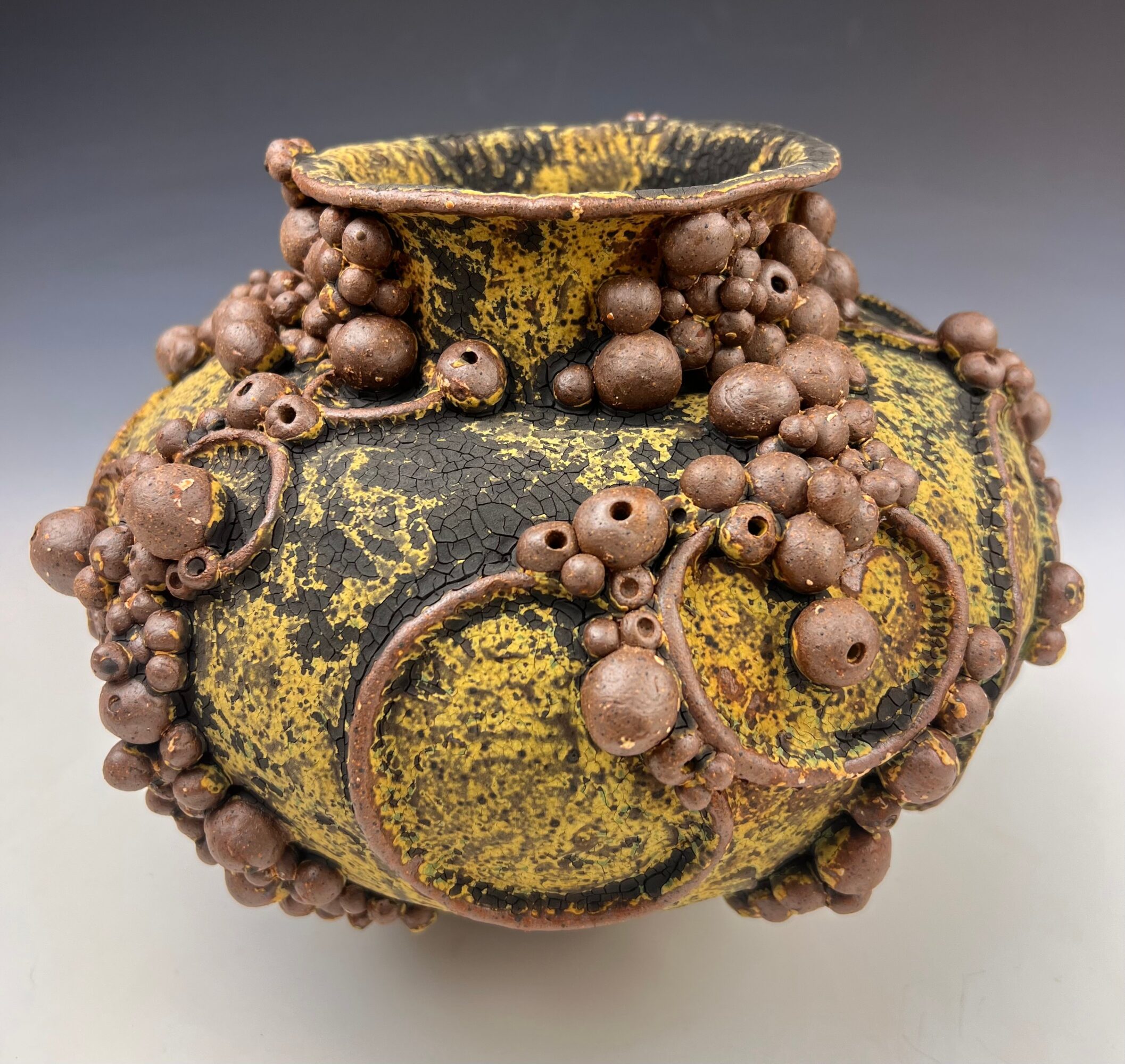Ancient ceramic vessel with a wide opening, decorated with numerous small, rounded protrusions and a yellow and black pattern.