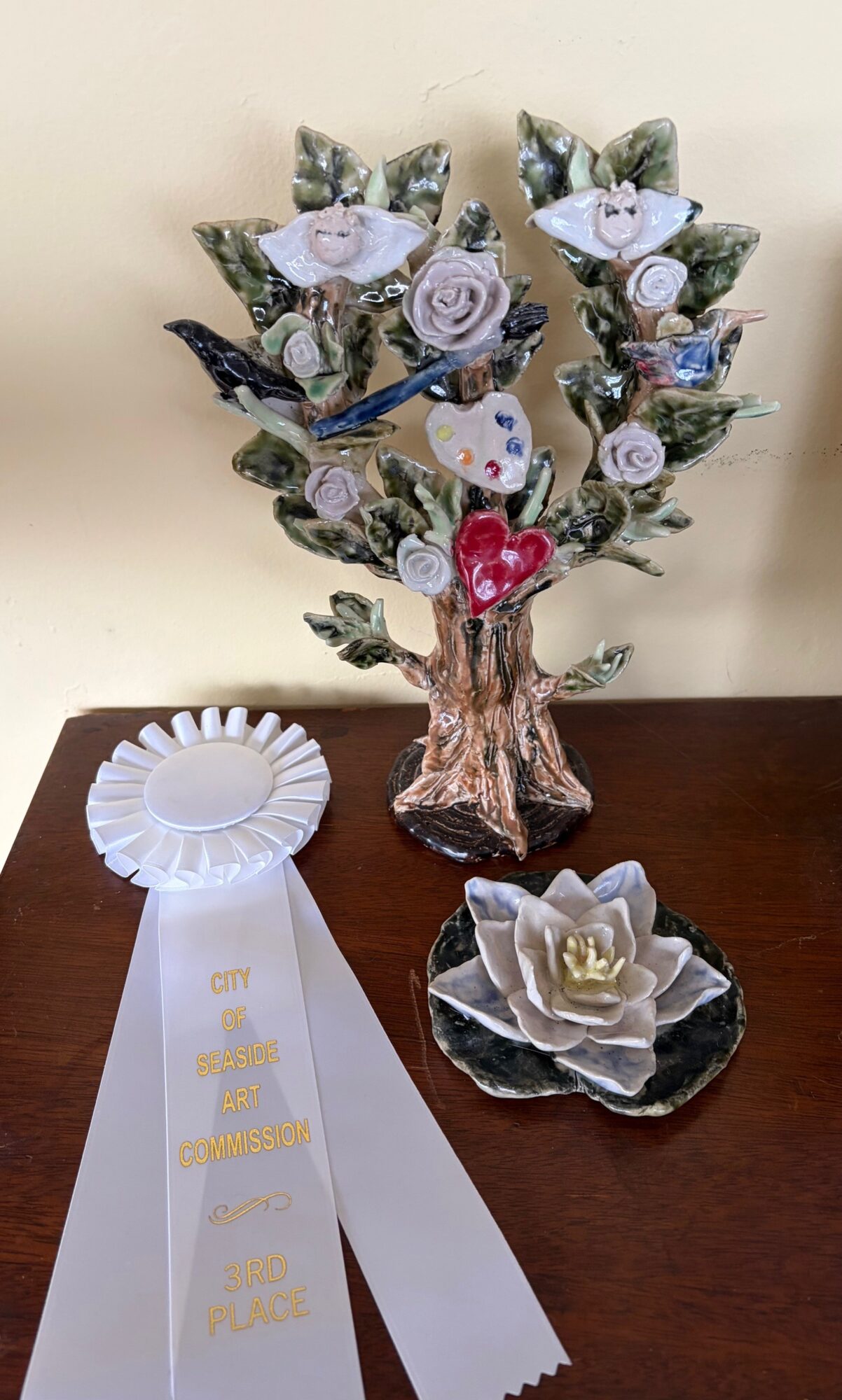 Decorative tree with purple and white flowers, a white ribbon with gold text, and a white flower on a black dish.