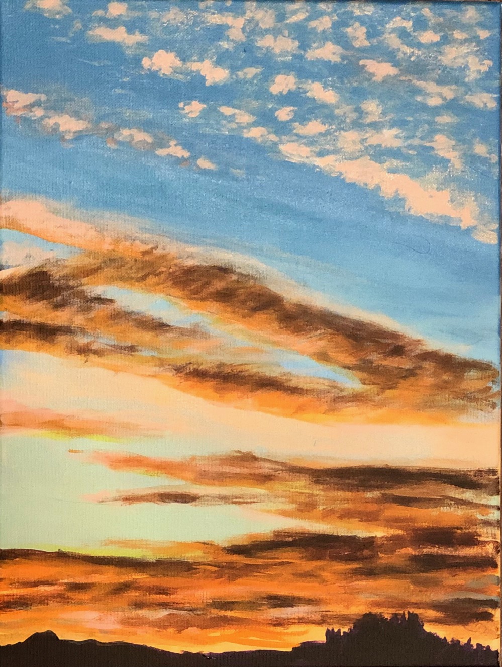 Colorful sunset sky with clouds in shades of orange, pink, and blue, and a silhouette of trees at the horizon.