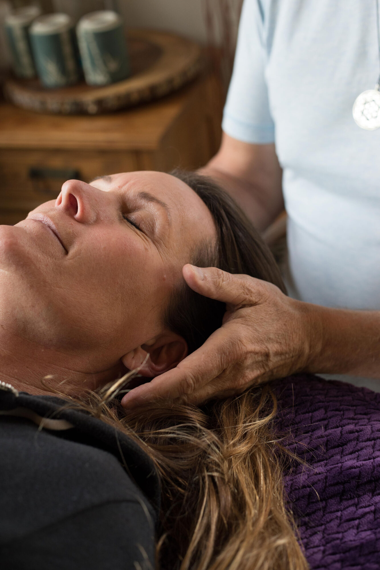 Woman receiving a facial massage with a therapist's hands on her face, lying down with eyes closed.