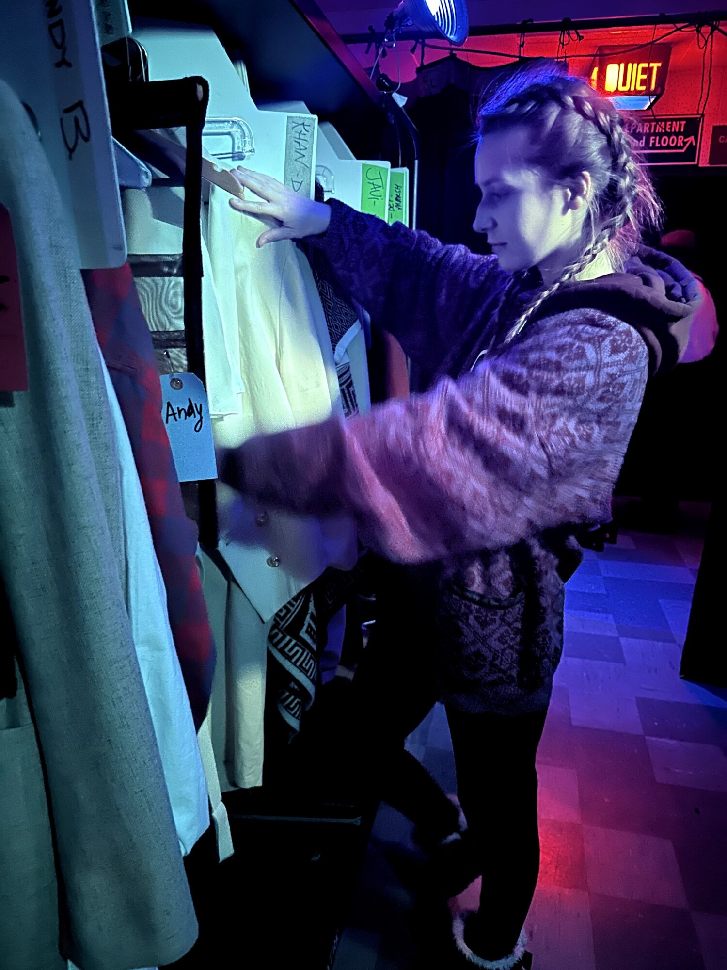 Person browsing fabric or clothing in a store, reaching for a white item, with colorful lighting and signs in background.
