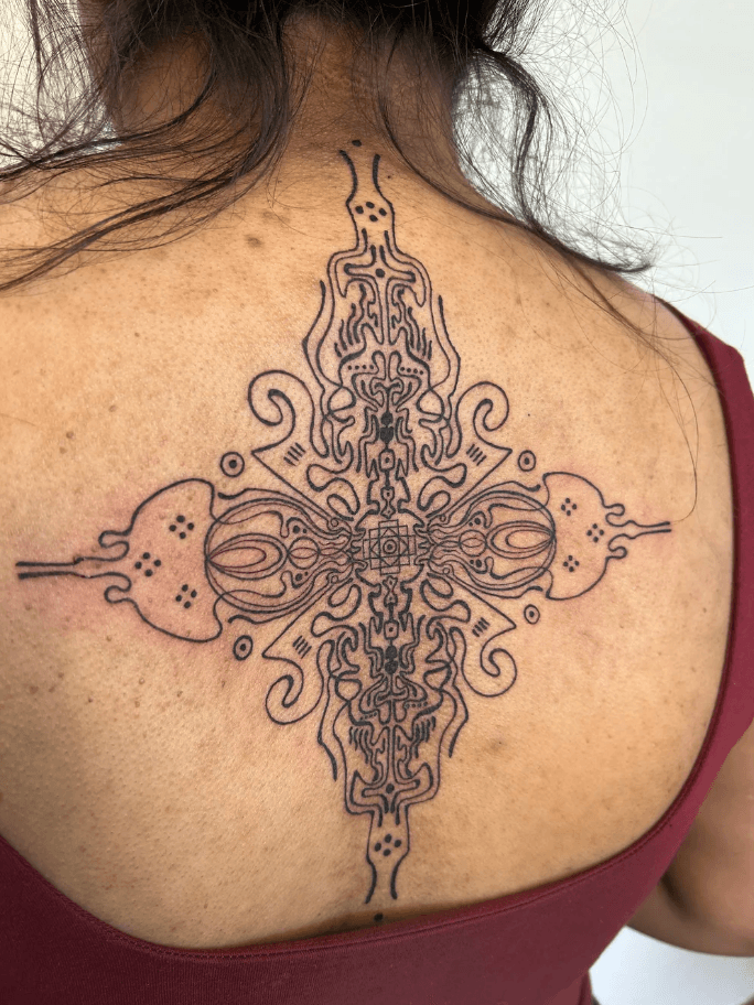 Intricate symmetrical tattoo on person's upper back with detailed line work and patterns.