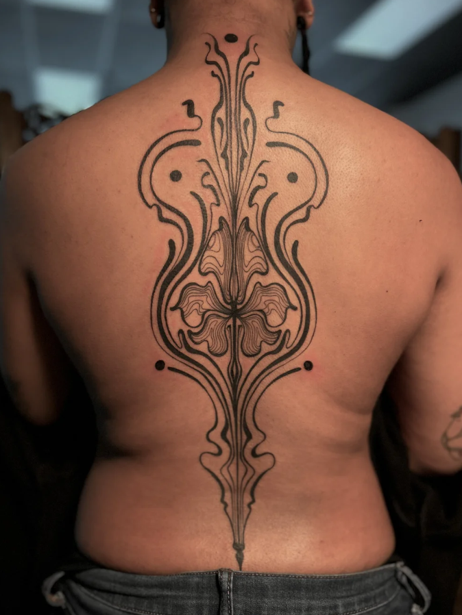 Intricate symmetrical black tattoo on person's back with floral and ornamental patterns, extending from upper to lower back.