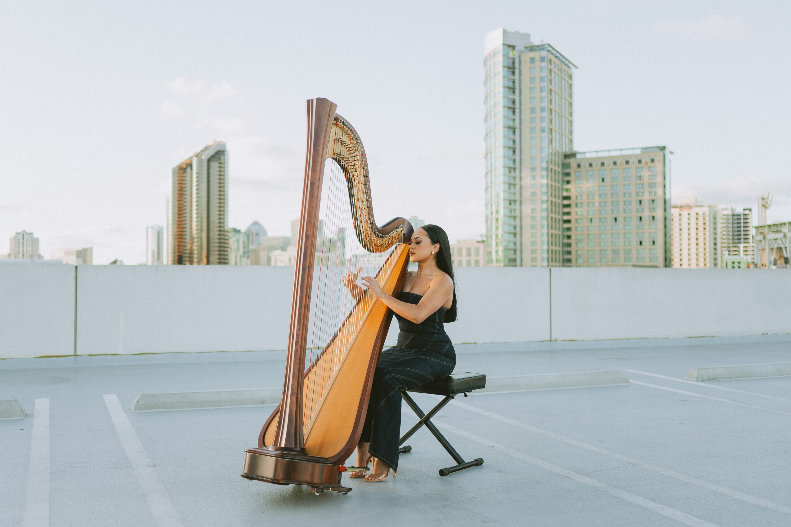Woman playing a harp on a rooftop with city buildings in the background.