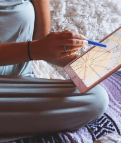 Person sitting cross-legged, using a tablet with a stylus, on a bed with a textured blanket.