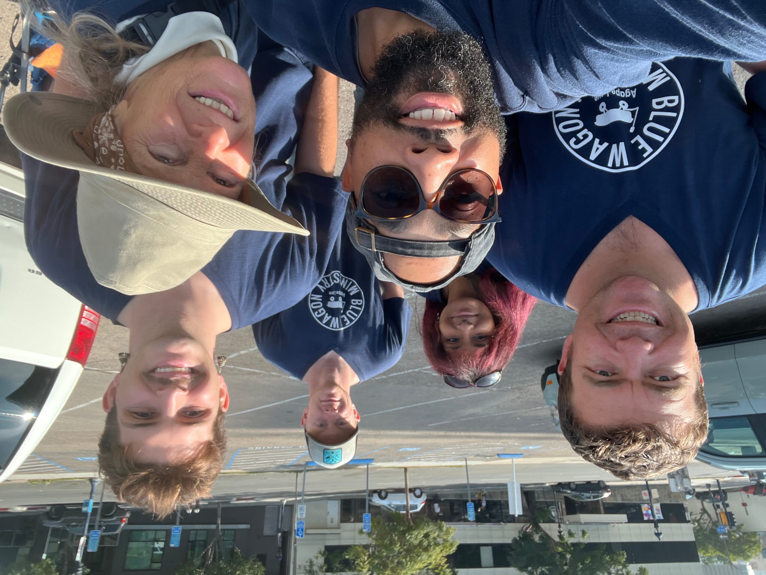 Group of five people smiling and taking a selfie outdoors, some wearing sunglasses and hats.