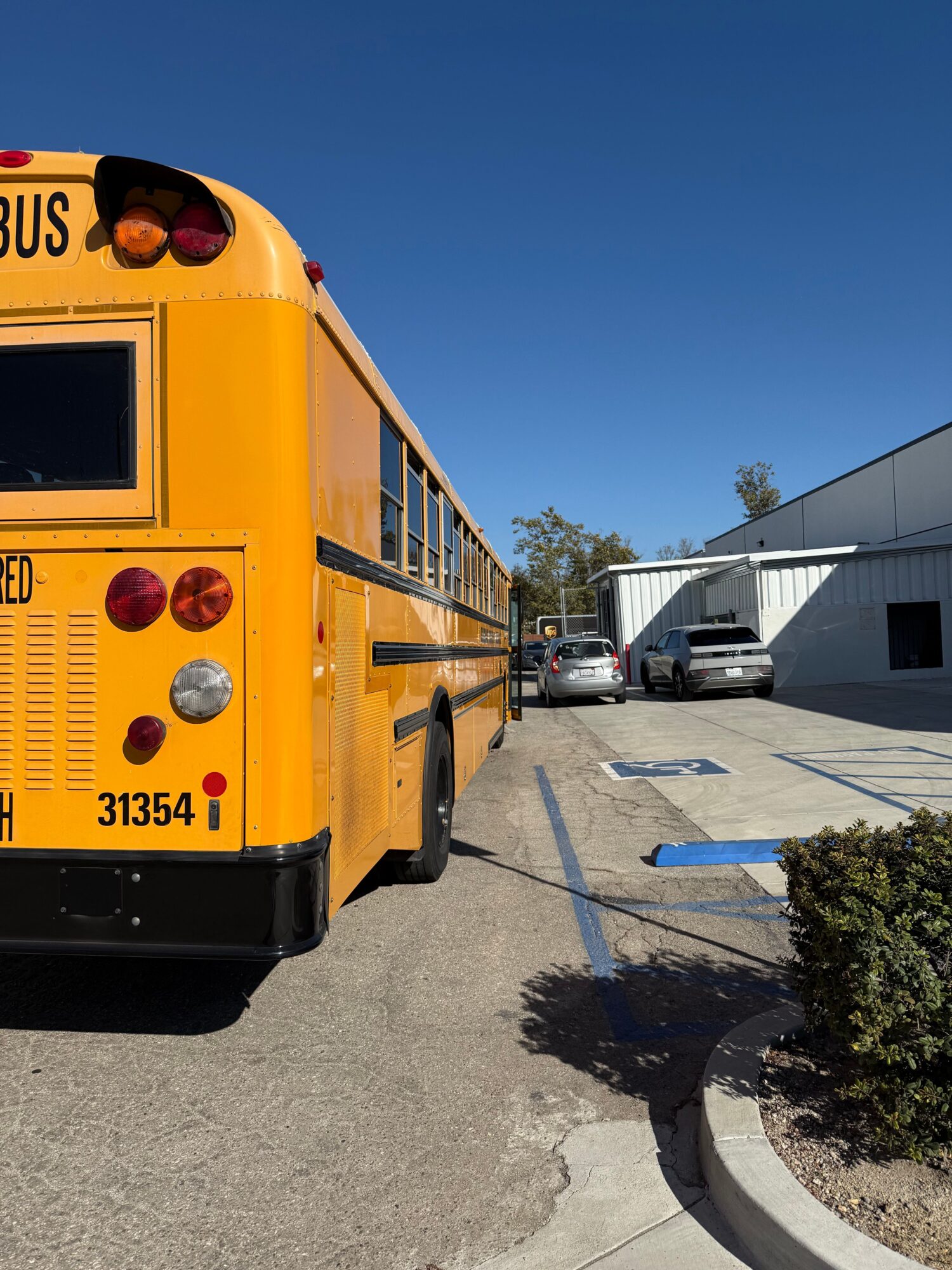 Yellow school bus parked in a lot with a building and trees in the background.
