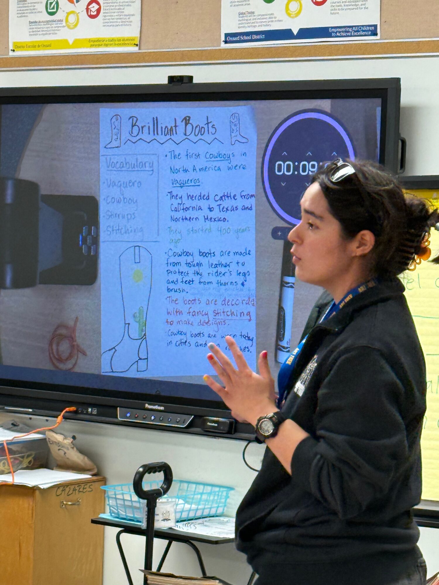 Woman presenting a handwritten poster on a digital screen in a classroom or office setting.