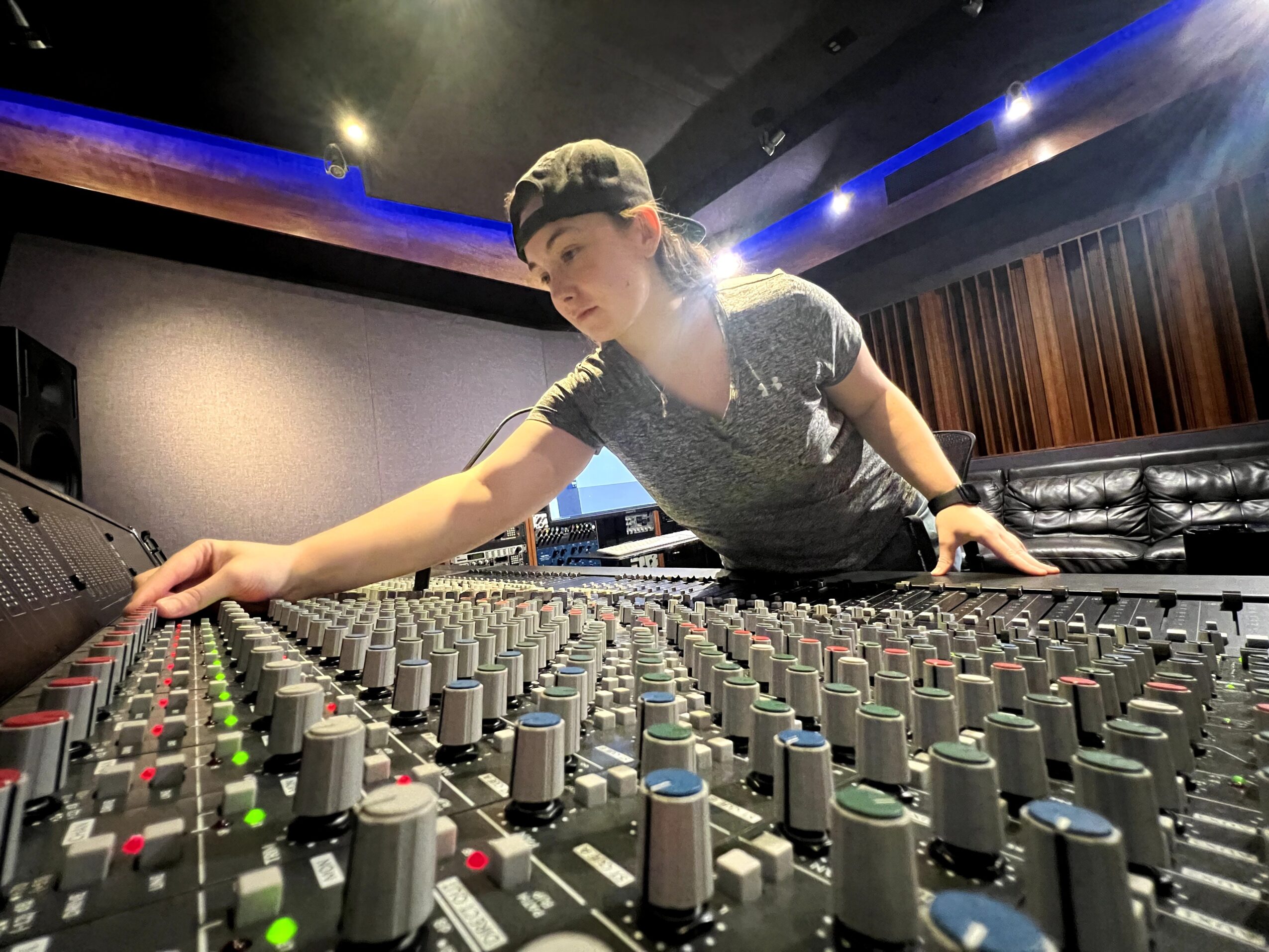 Person adjusting audio mixer in a recording studio with dim lighting and wooden wall panels.