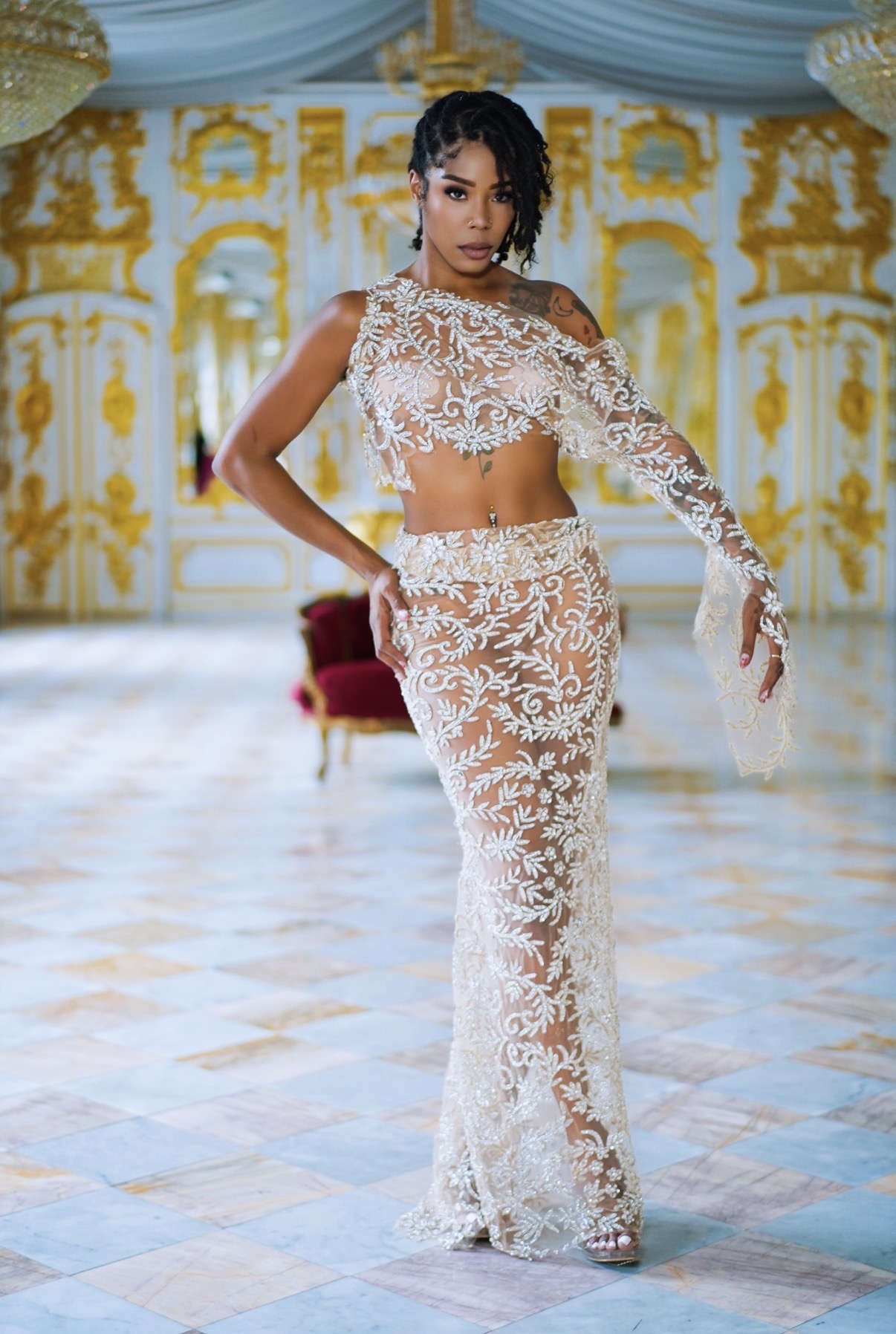 Woman in white lace outfit standing in ornate room with gold and blue decor, posing with hand on hip.