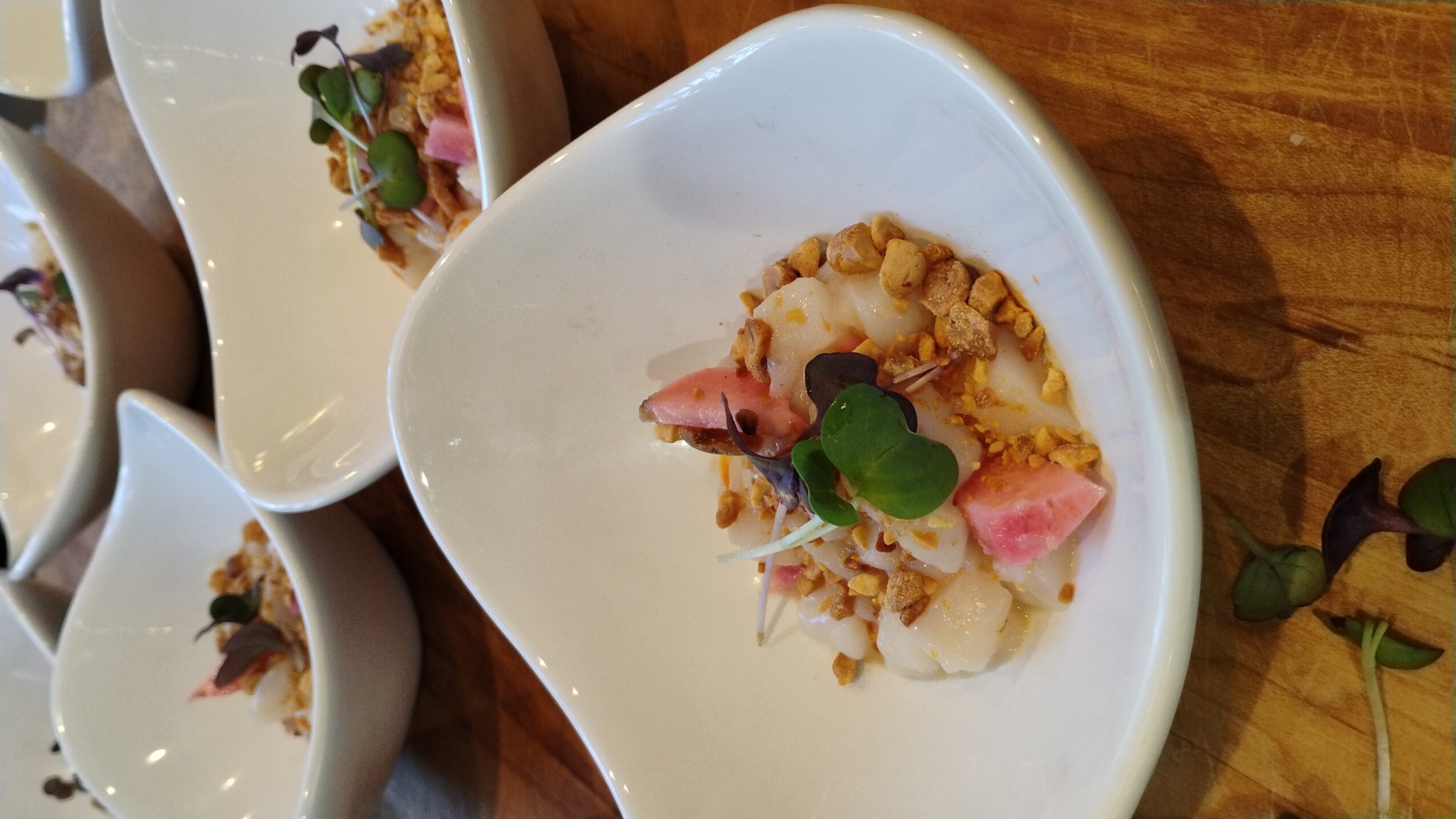 Dish with rice, pink slices, and green garnish in a white bowl on a wooden table.
