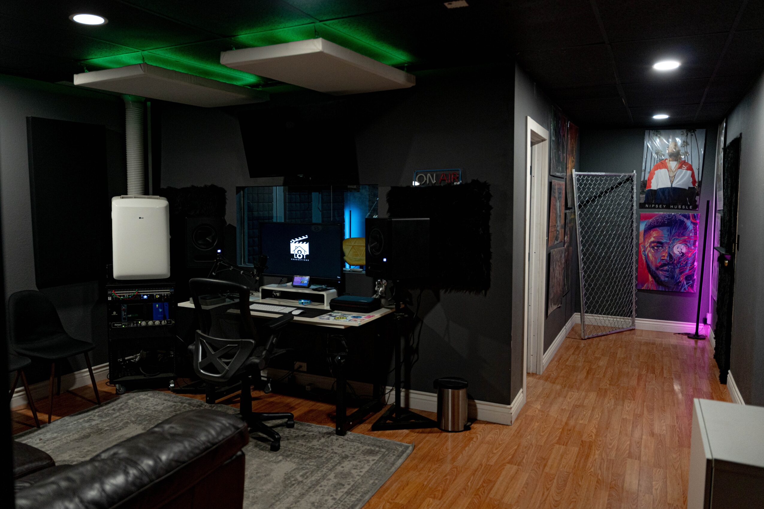 Dark room with computer setup, chairs, and colorful lighting, leading to a hallway with artwork and a chain-link fence.