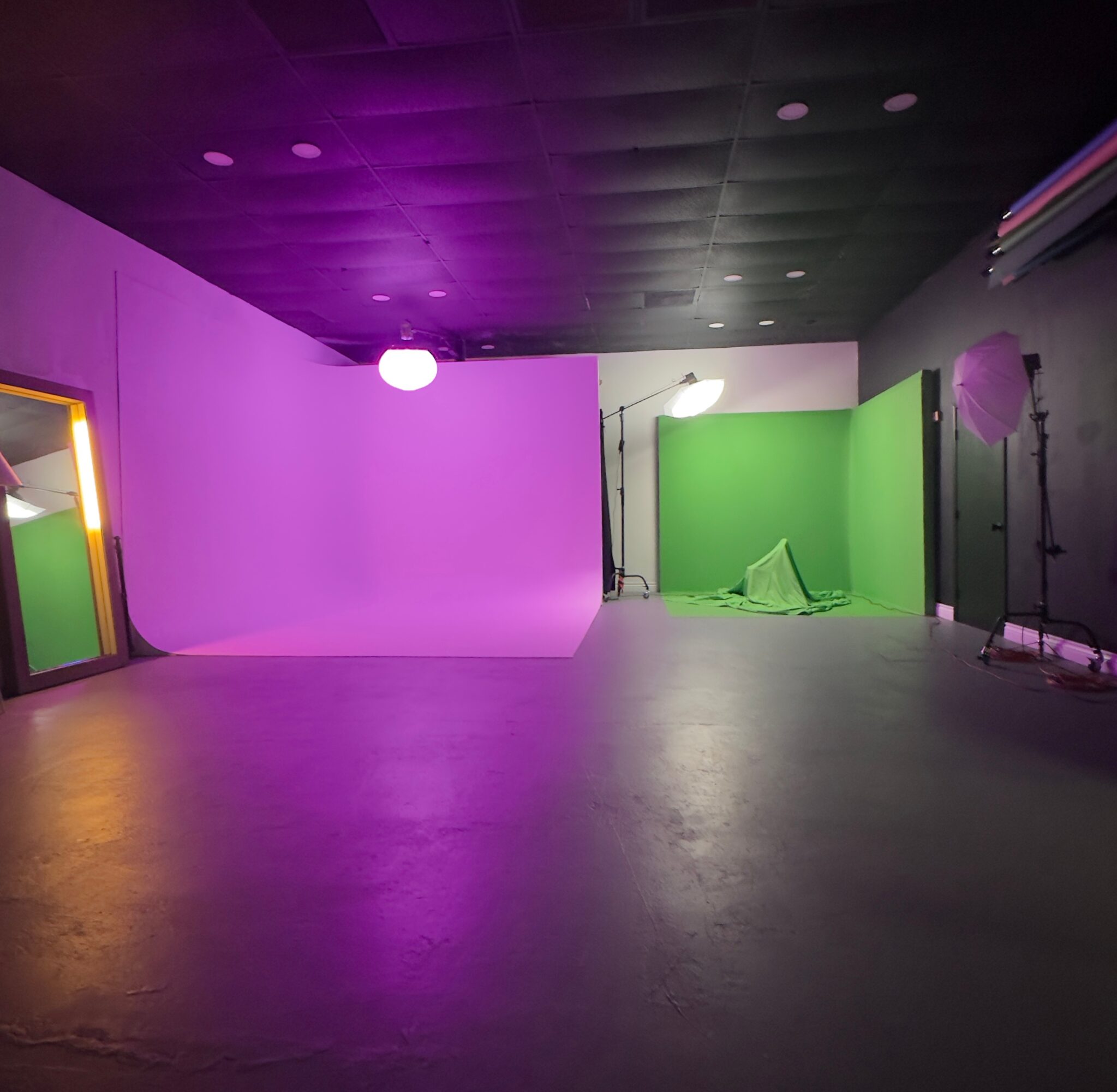 Photography studio with purple and green backdrops, lighting equipment, and a reflective floor.