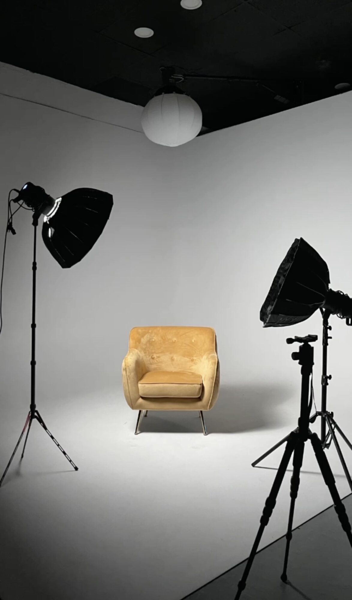Studio with a yellow armchair, two large studio lights, a white ceiling light, and a white background.