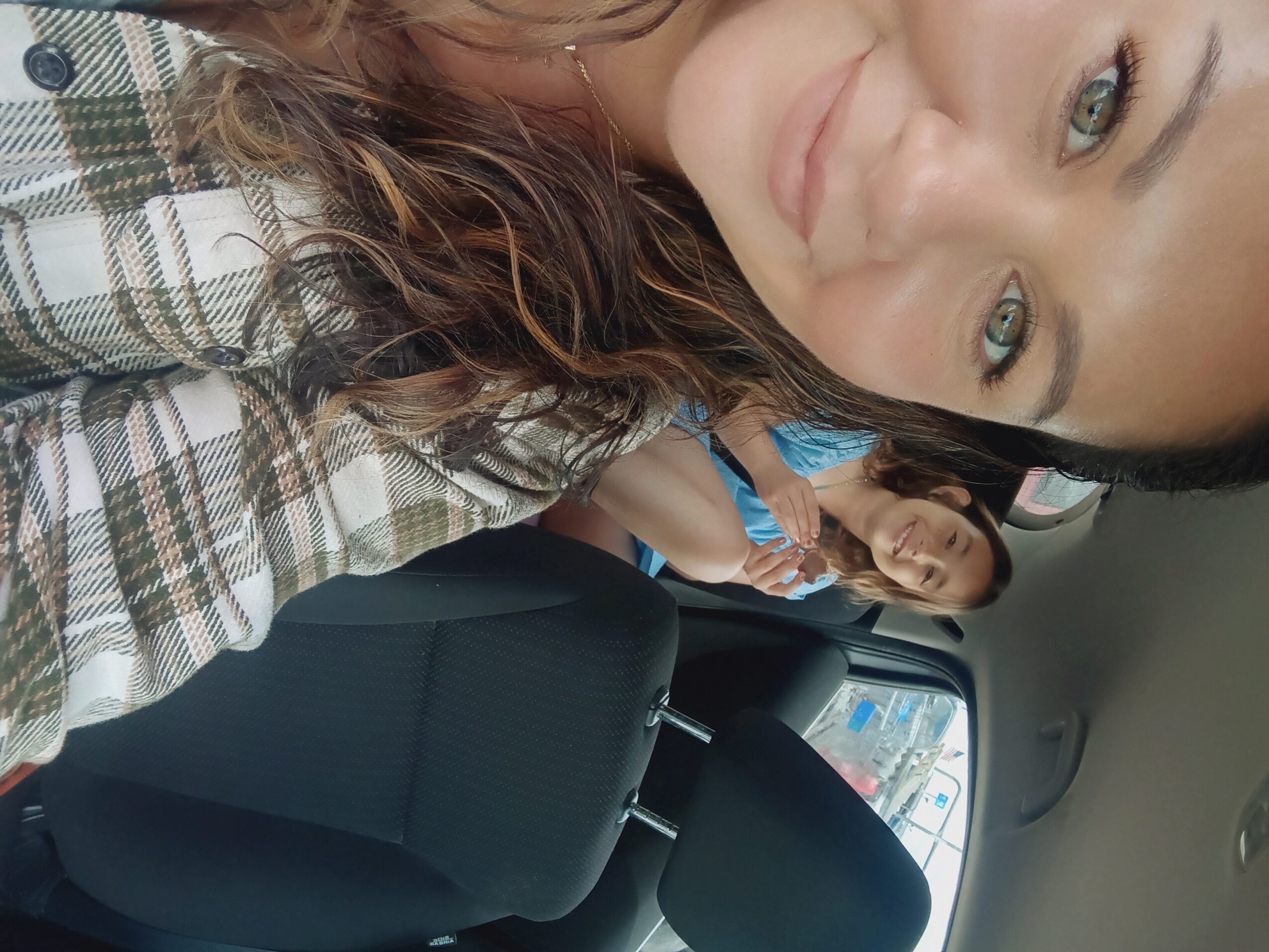 Two women sitting in a car, one taking a selfie, with a seat and window visible in the background.