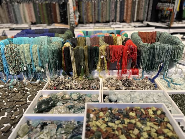 Display of colorful yarns and beads in a store, with shelves of books in the background.