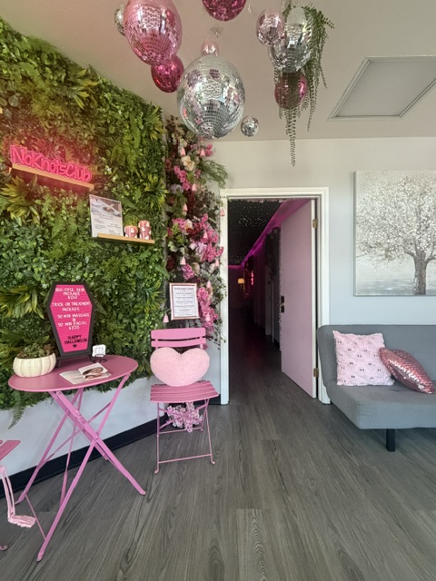 Pink-themed indoor space with pink furniture, decorations, and greenery, including a pink table, chairs, and ornaments.