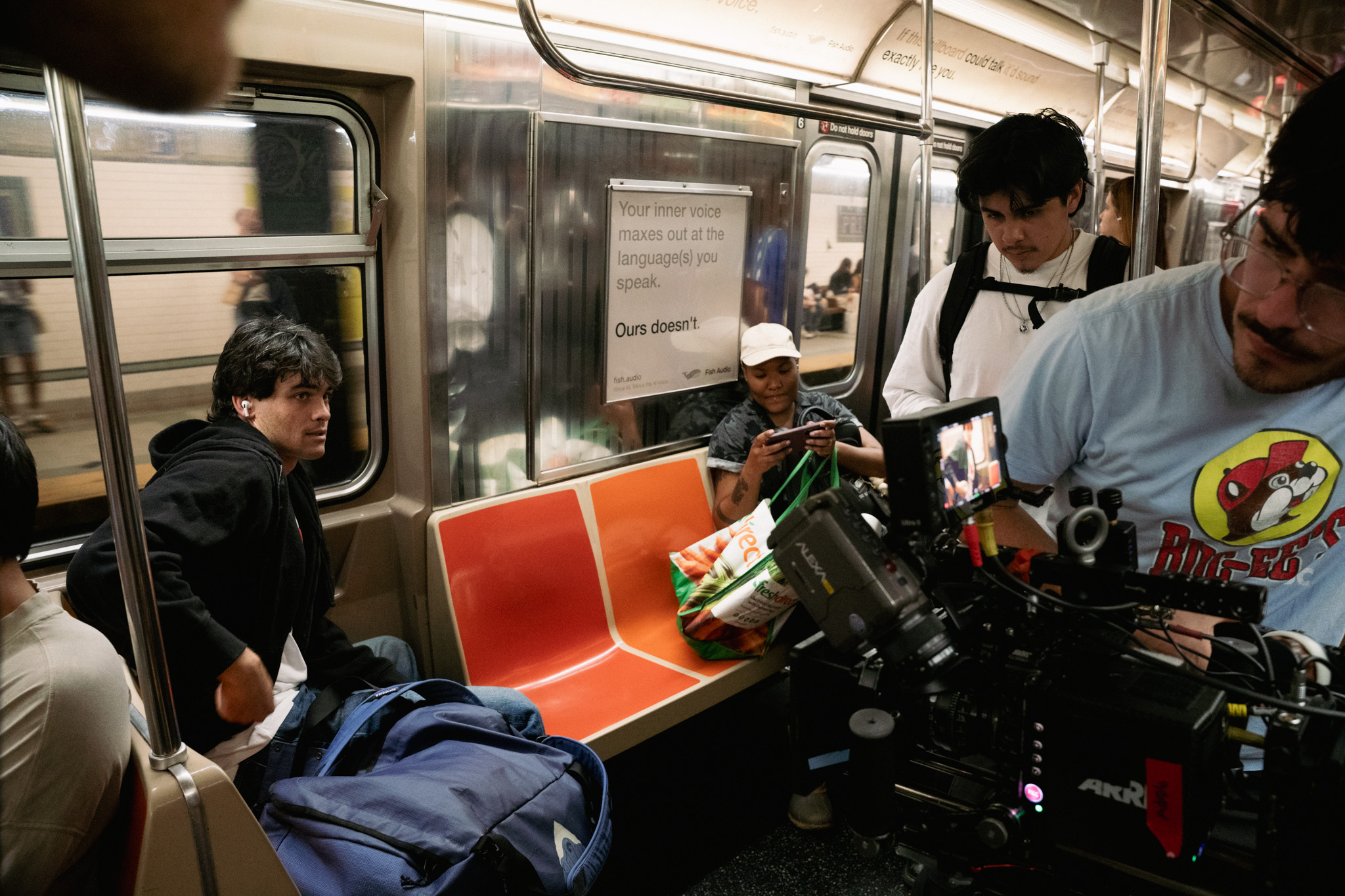 People sitting and standing inside a subway train, some using cameras, with orange seats and metallic walls.