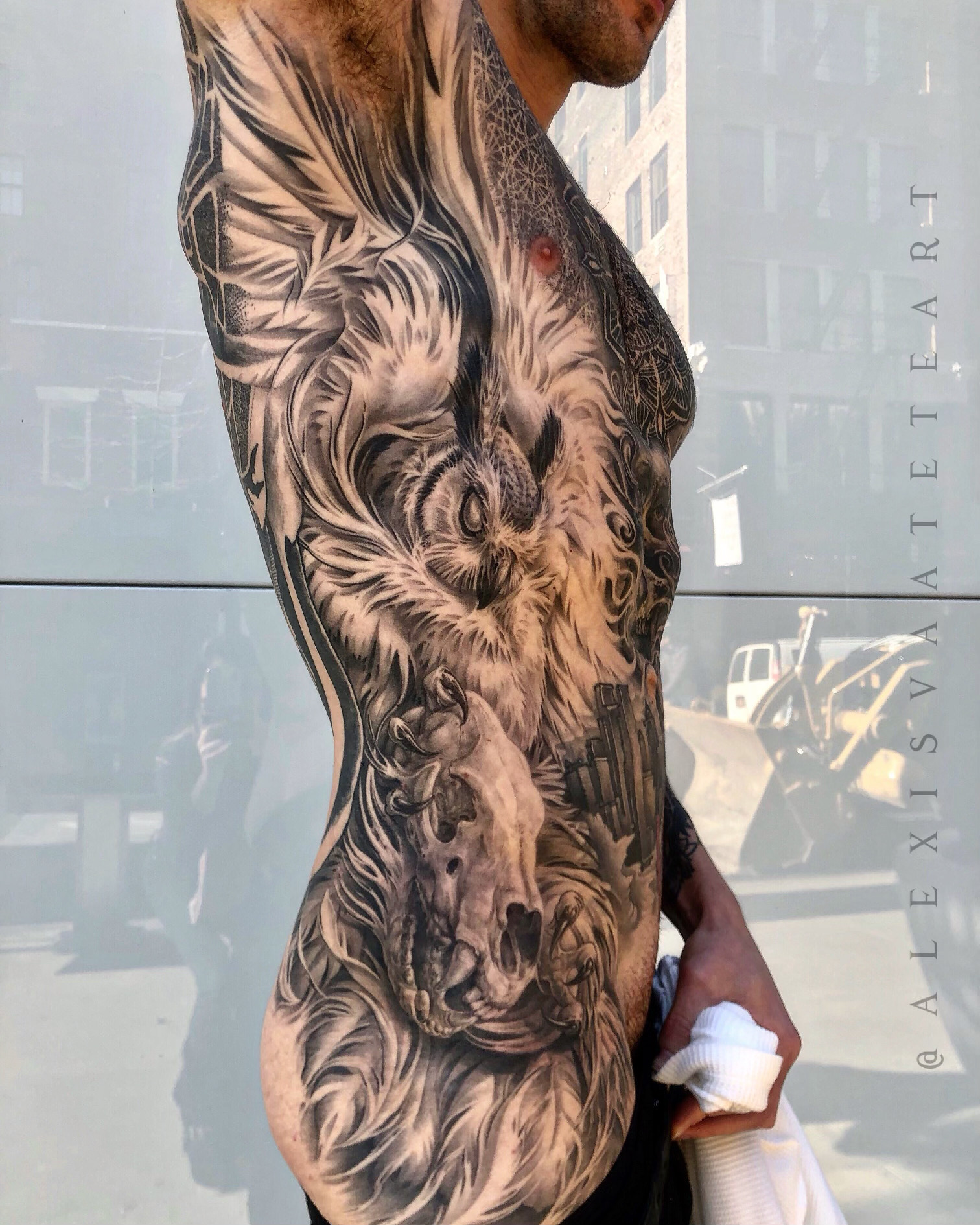 Side view of a person with a detailed lion tattoo covering the chest and arm, holding a tissue, in front of a window.