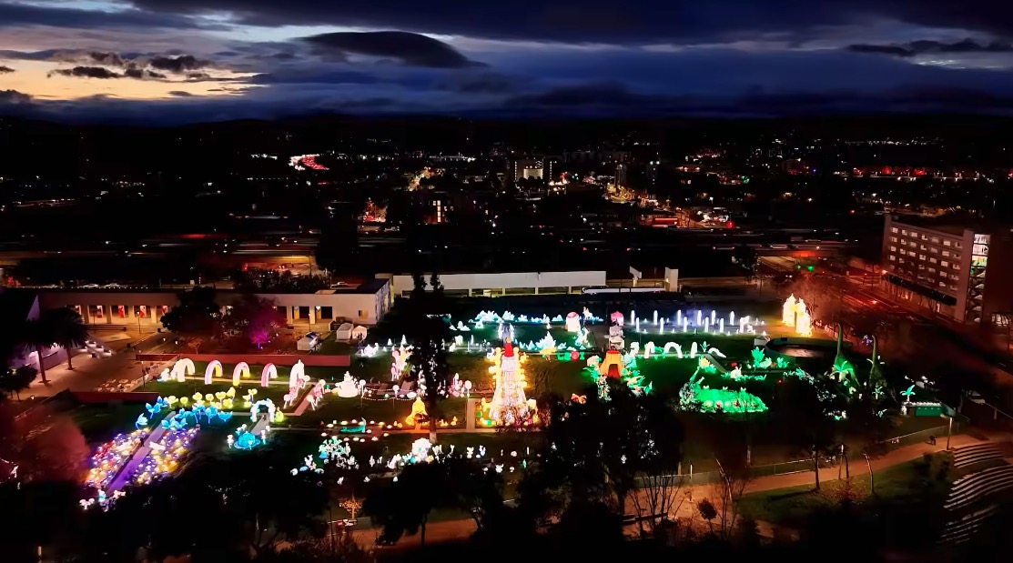 Nighttime cityscape with colorful holiday lights, buildings, and a dark sky with clouds.
