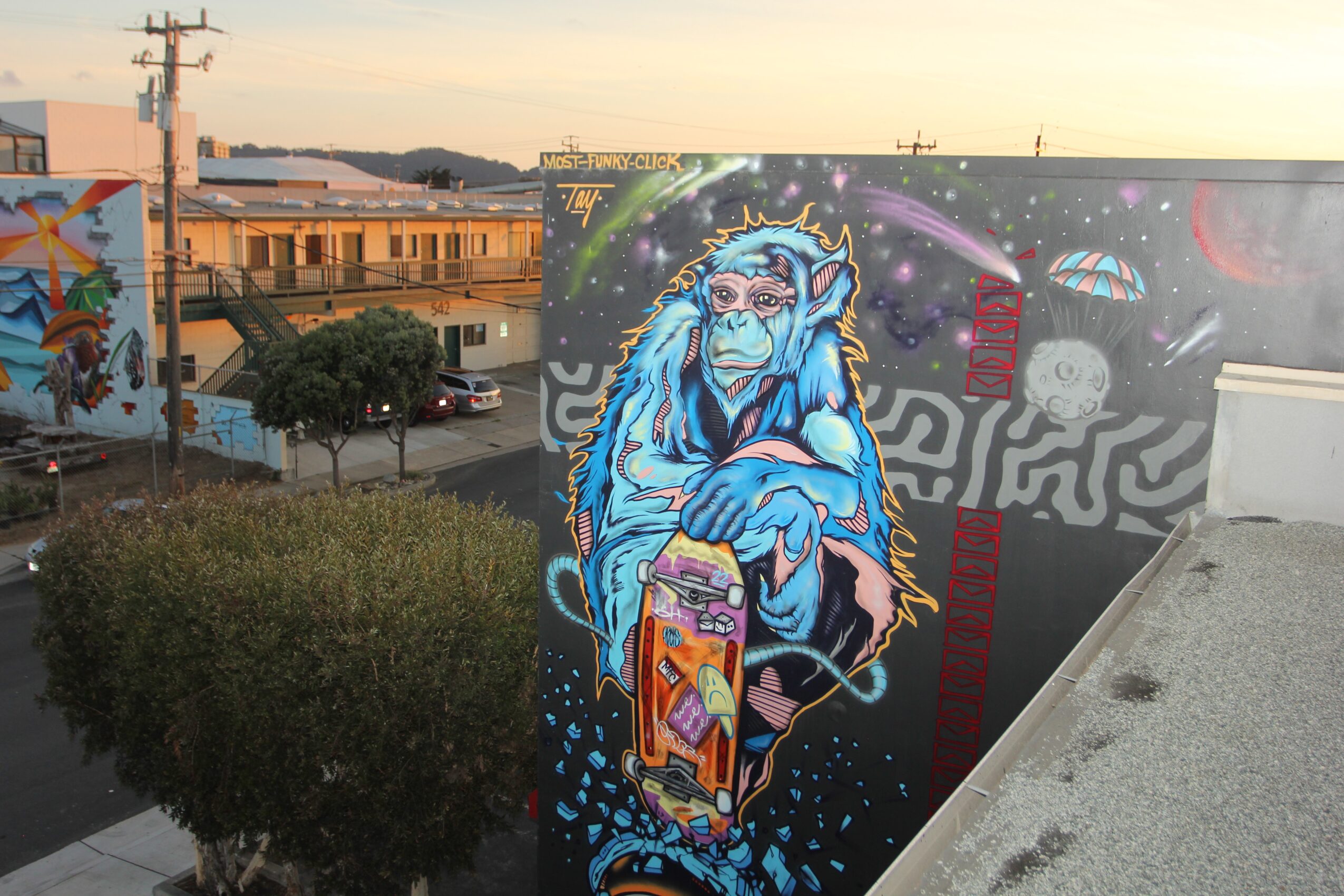 Colorful mural of a blue monkey with a cosmic background, holding a skateboard, on a city wall.