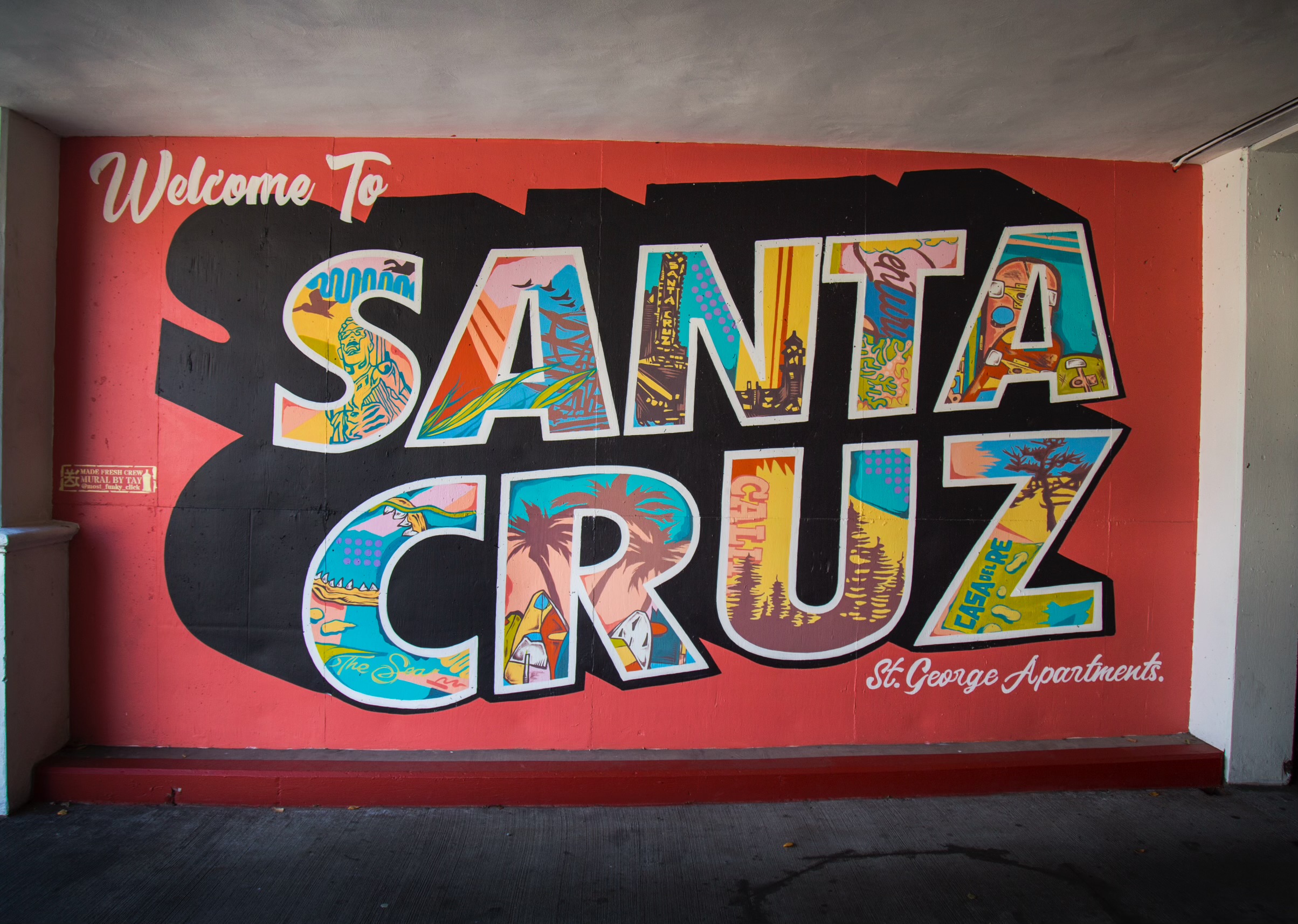 Colorful mural with large letters spelling Santa Cruz, with a red background and welcoming message.