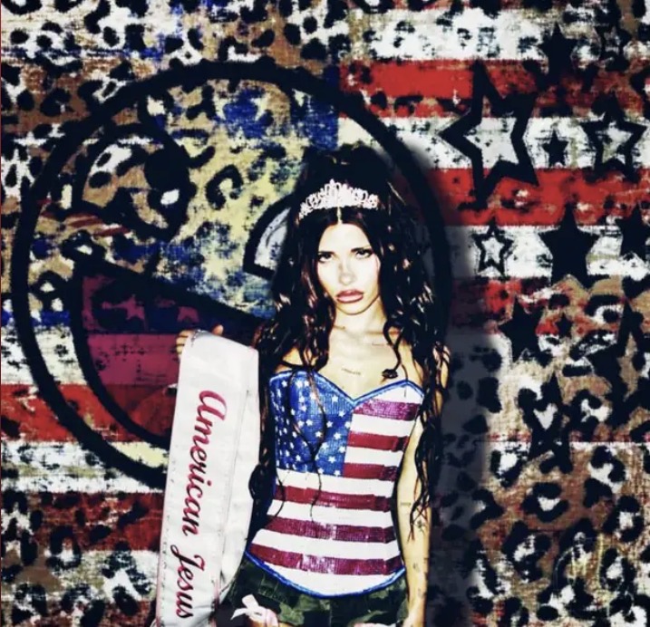 Young woman with long dark hair wearing a tiara and patriotic outfit, standing in front of a colorful graffiti wall.