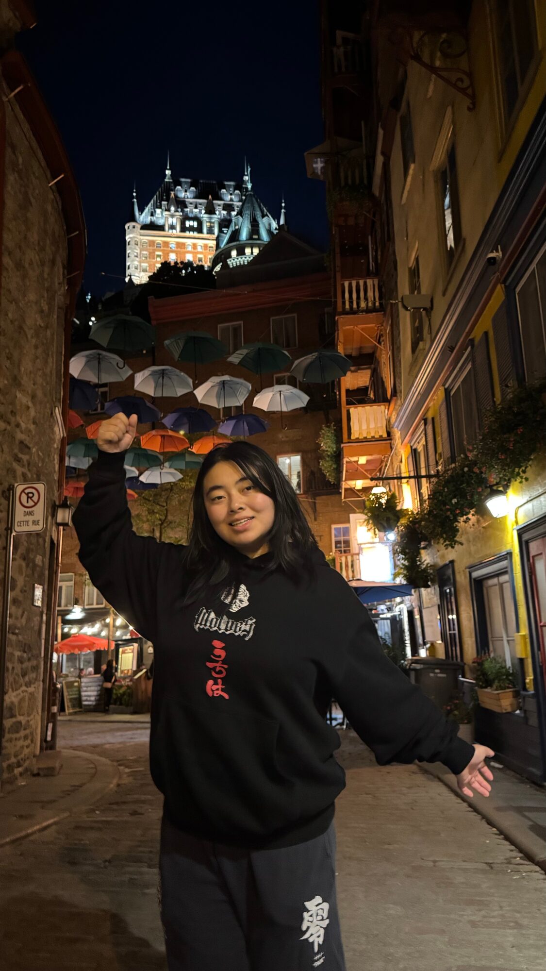 Young woman standing on a city street at night, holding umbrellas, with a castle-like building illuminated in the background.