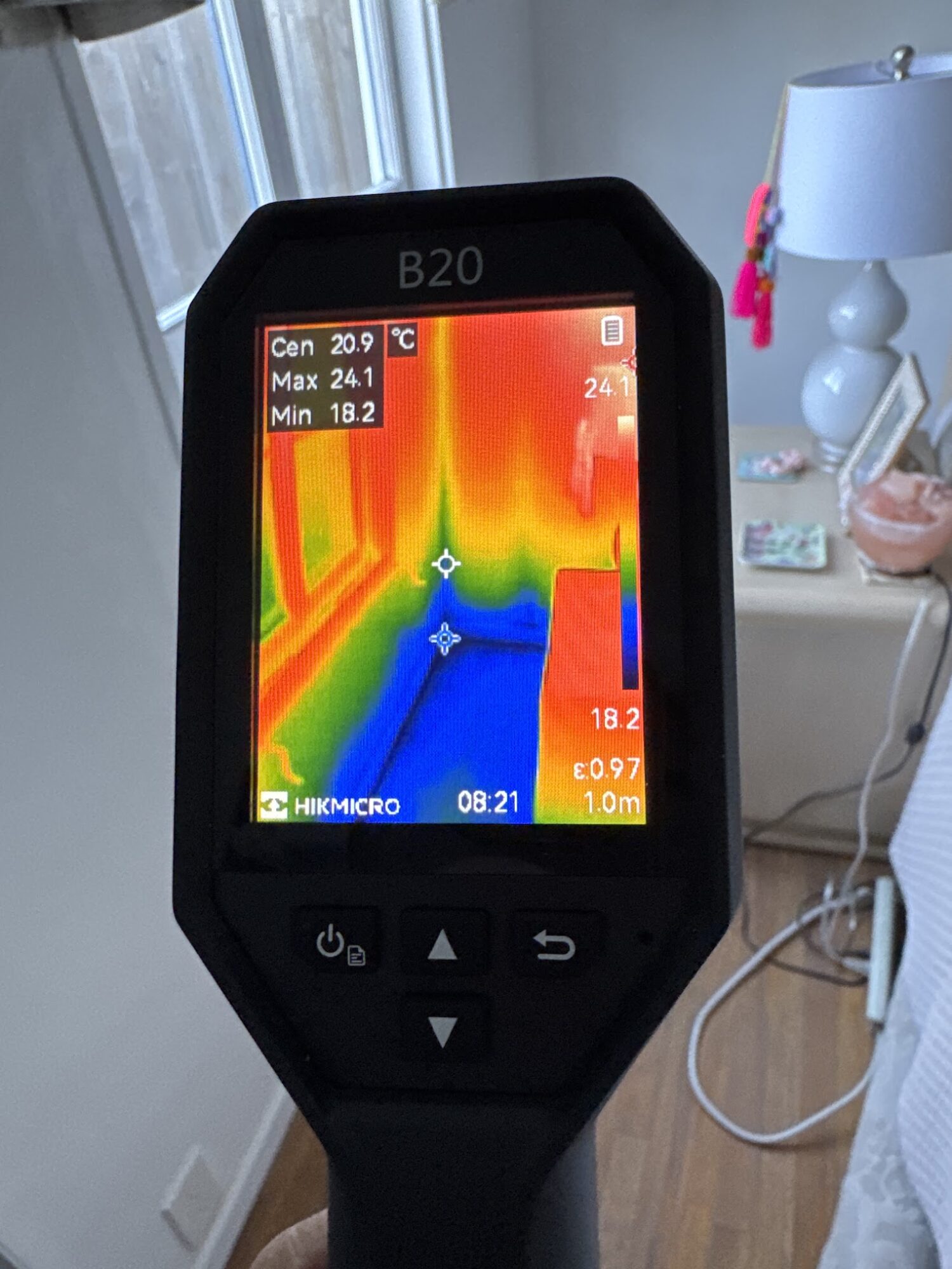 Thermal imaging device showing a color gradient of temperature variations in a room, with a white arrow pointing forward.