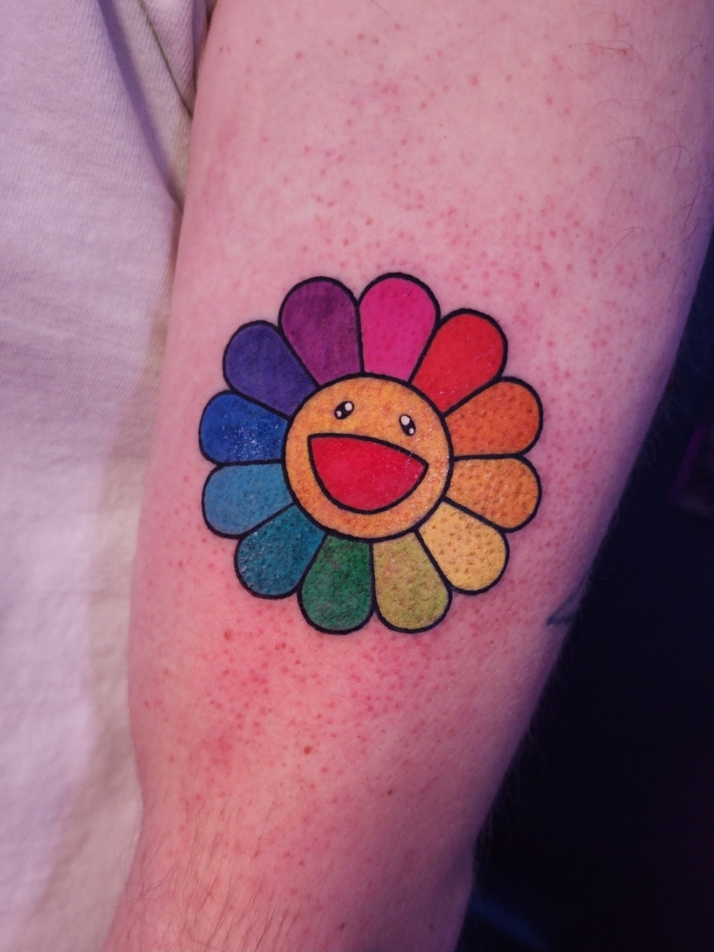 Colorful flower with a smiling face, rainbow petals, on skin with red spots.