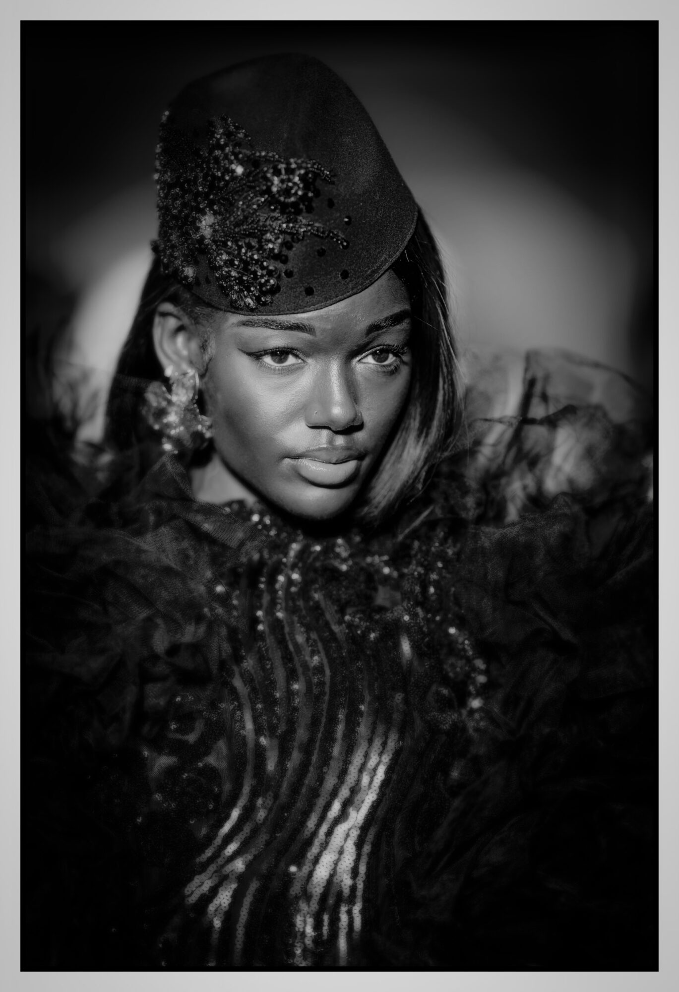 Portrait of a woman wearing a decorative hat and elaborate clothing, looking directly at the camera, in black and white.