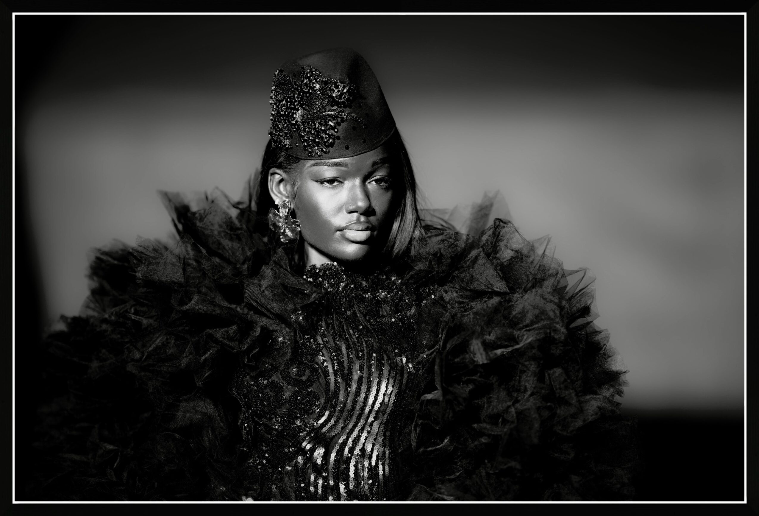 Woman wearing a feathered black outfit and a hat, looking to the side, in black and white.