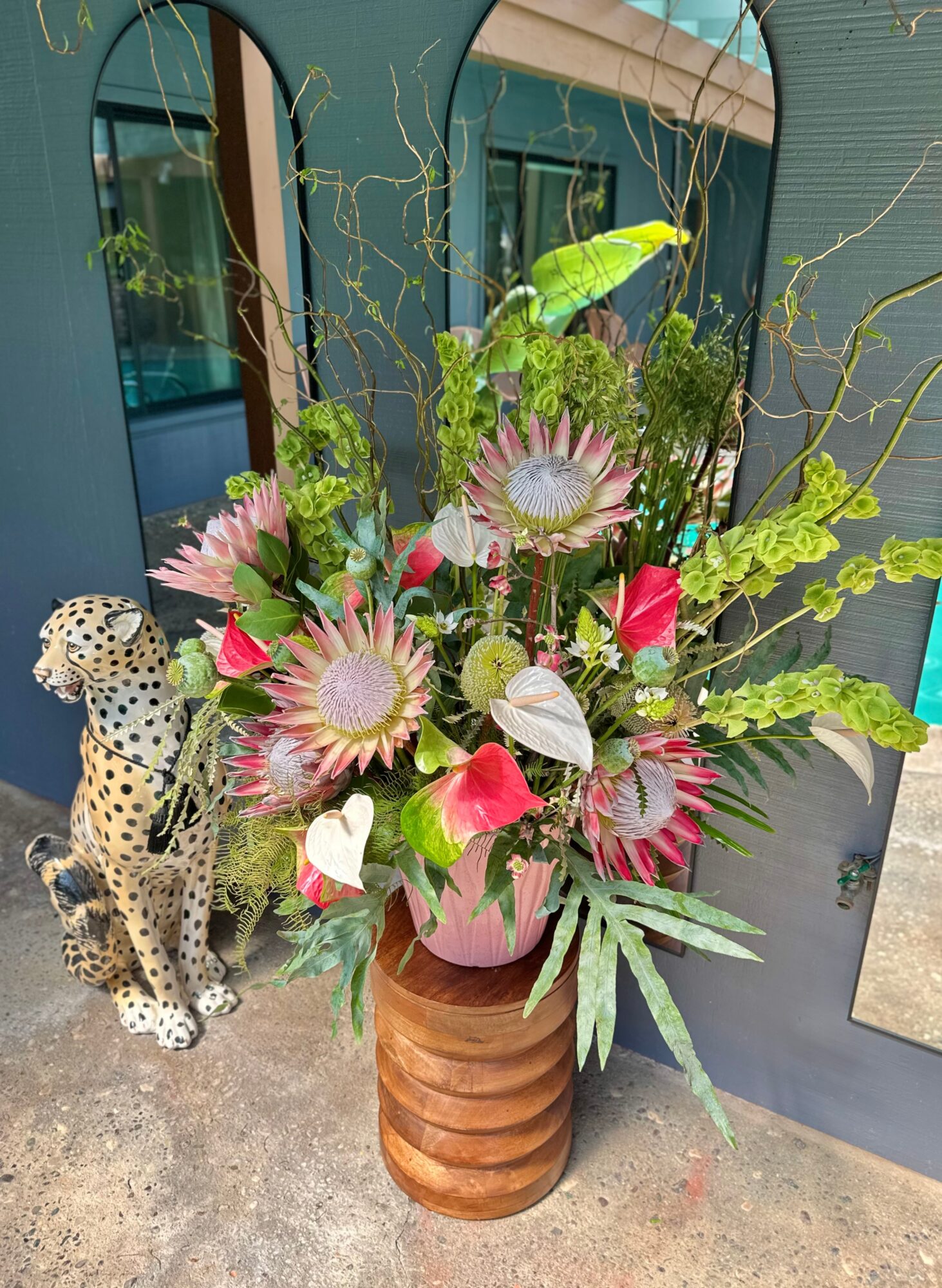 Large colorful flower arrangement in a brown vase with pink, white, and green flowers, and a leopard figurine beside it.