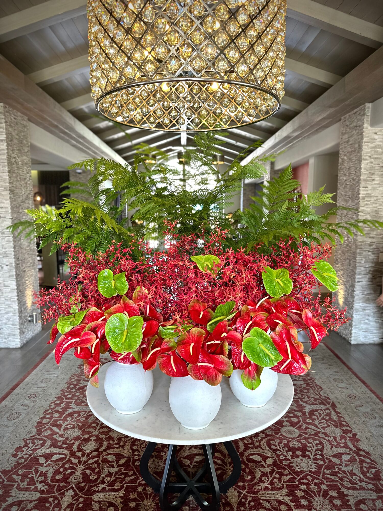 Large floral arrangement with red and green plants on a round table in a spacious indoor setting.