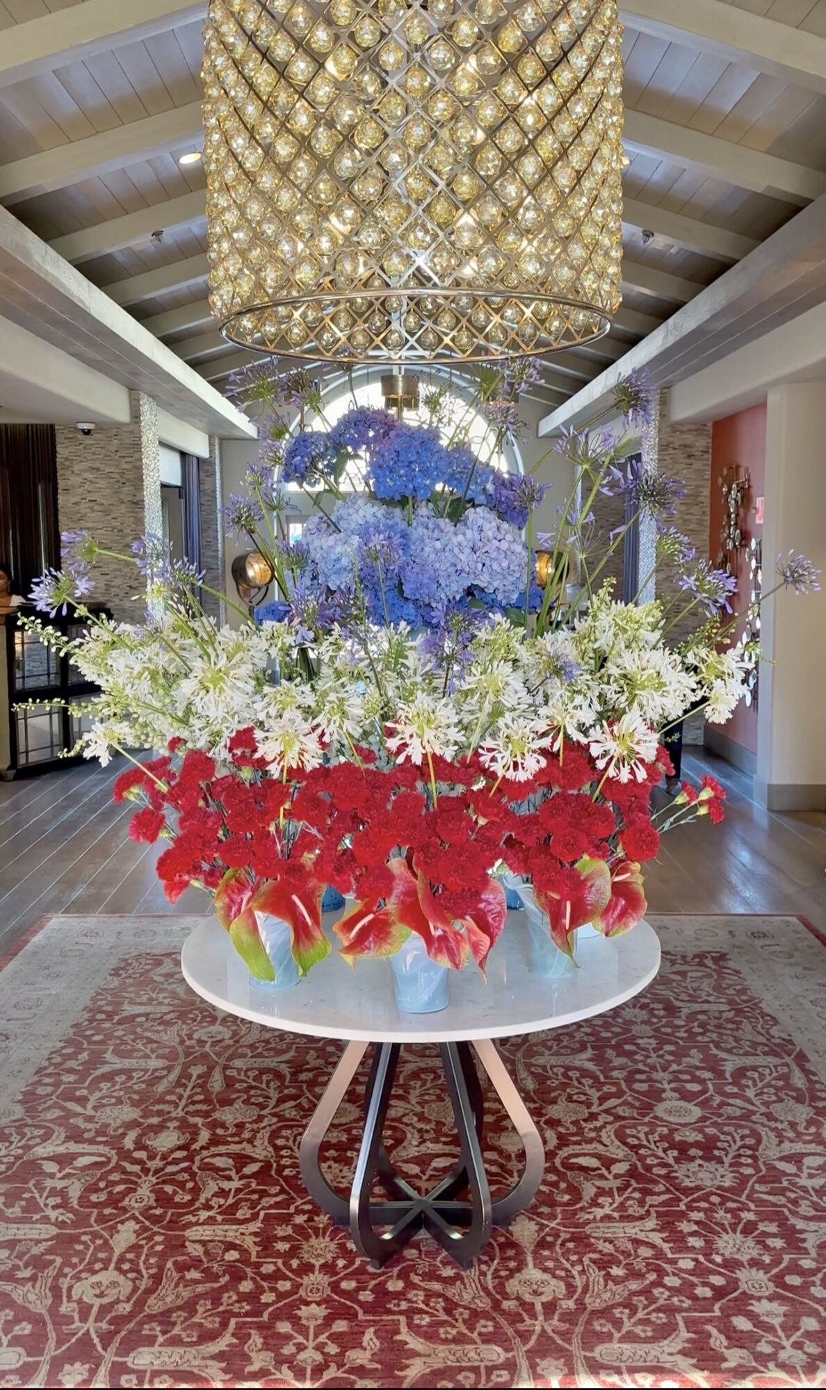Elegant floral arrangement with red, white, and blue flowers on a round table in a decorated interior space.