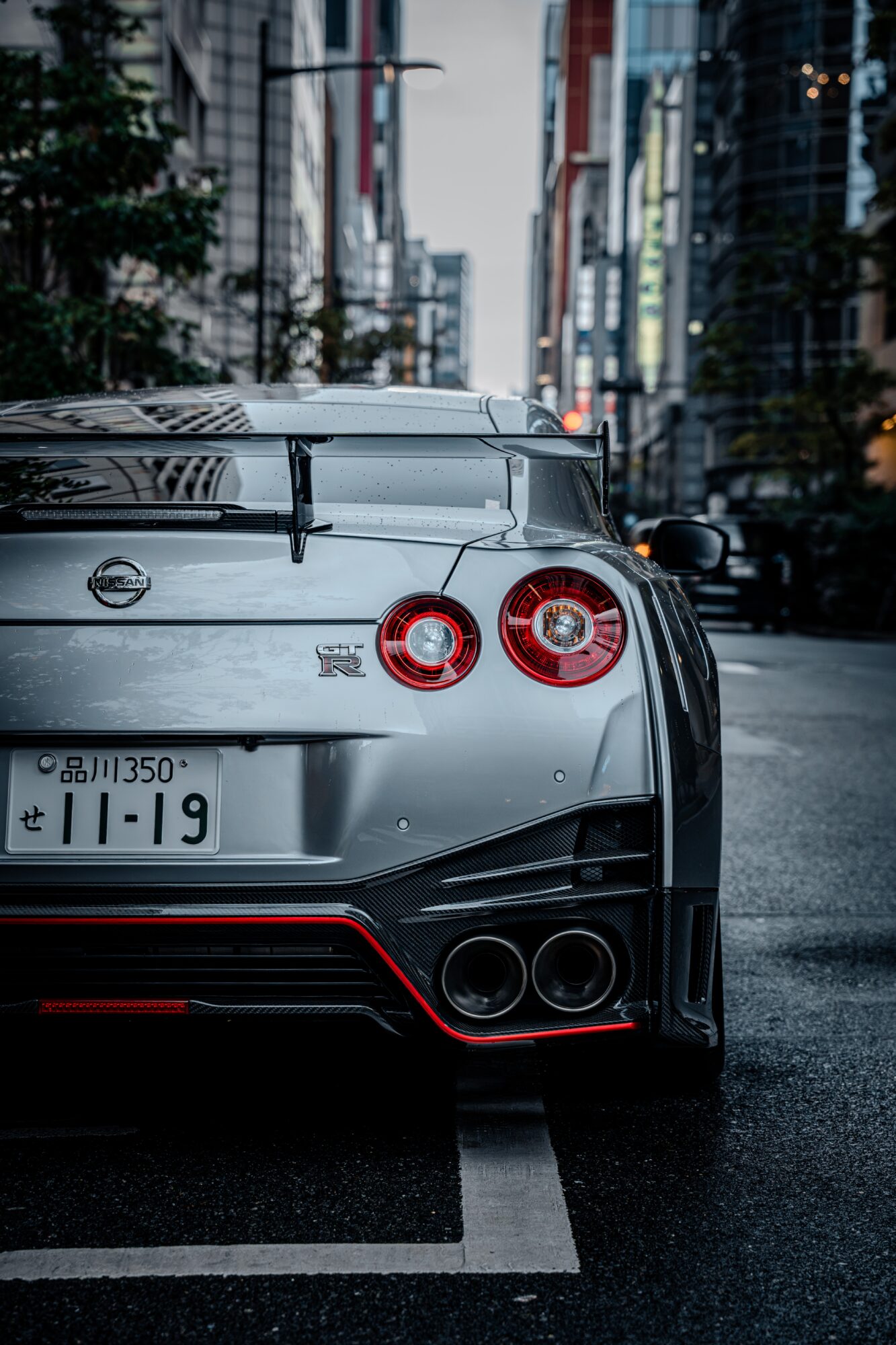Silver sports car parked on city street with buildings and traffic in background.