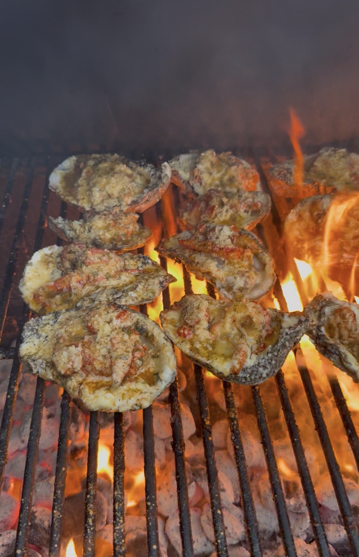 Fried oysters cooking on a grill with flames and smoke, with a metal grate below.