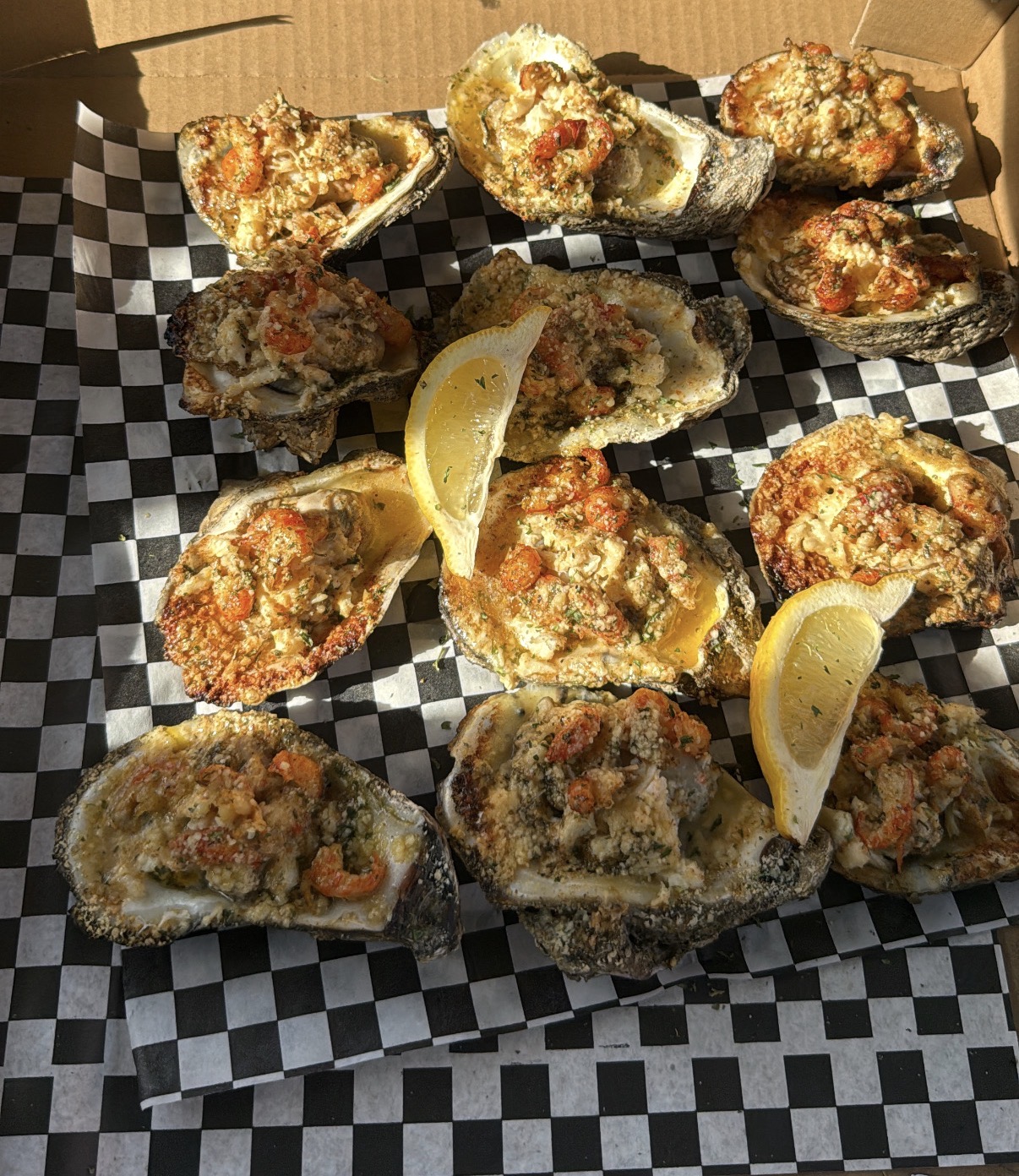 Oysters topped with breadcrumbs and garnished with lemon wedges on checkered paper.