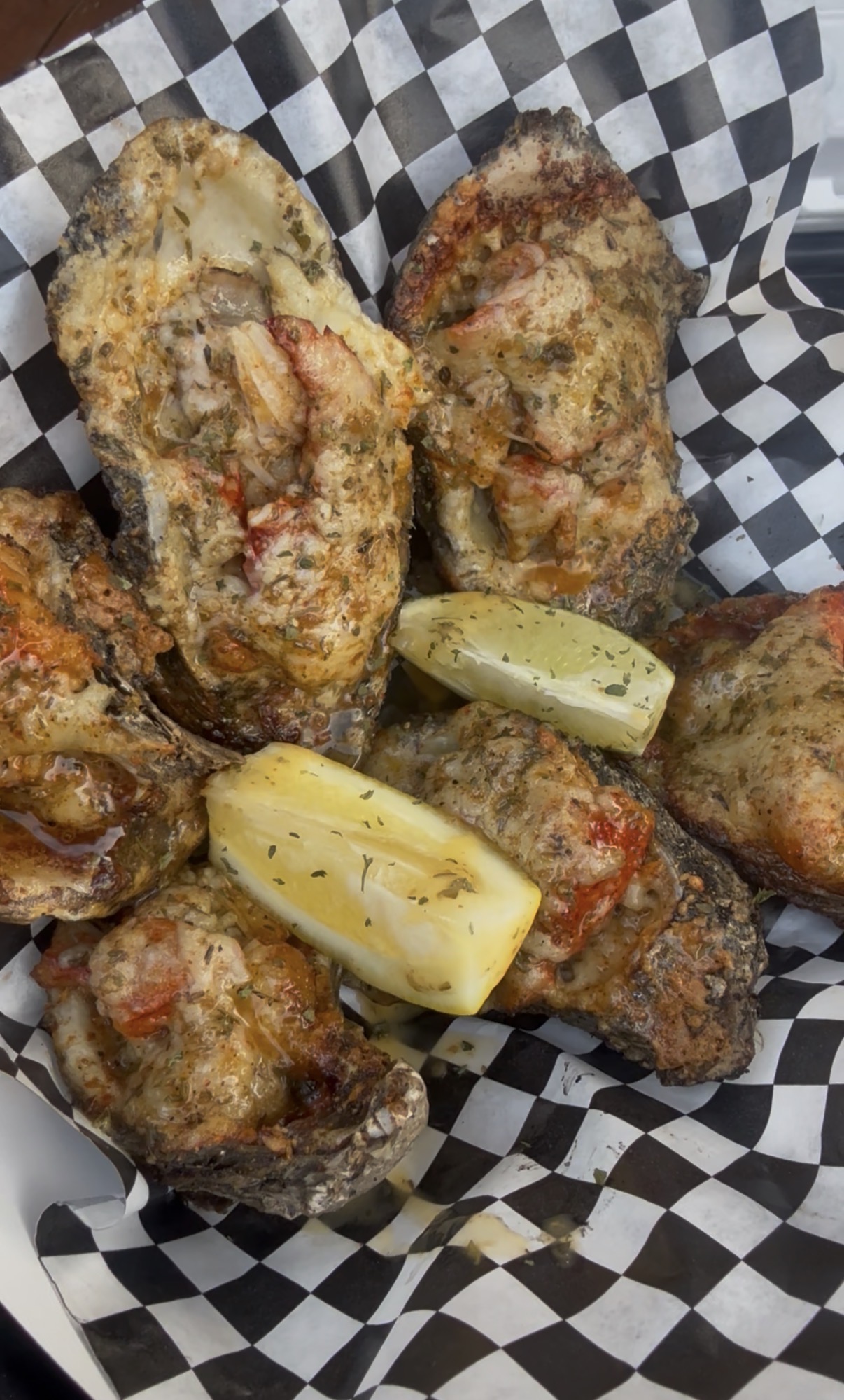 Fried oysters with lemon wedges on checkered paper, crispy and golden brown, garnished with herbs.